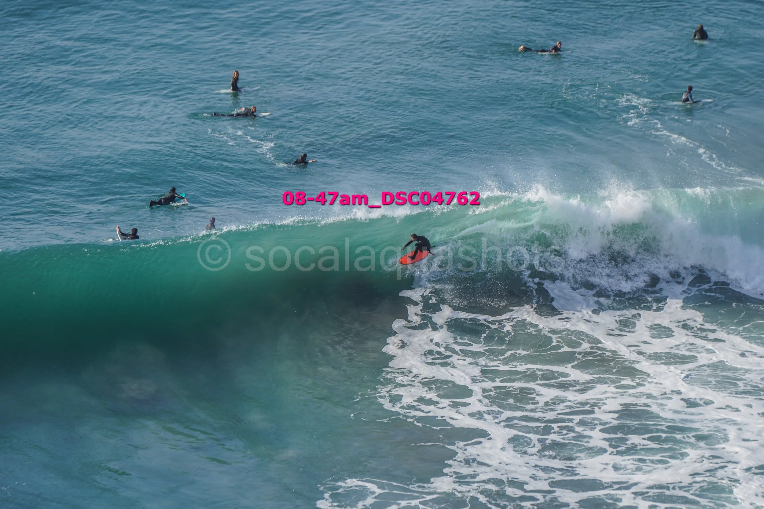 Surfer riding a large wave with several surfers in the water nearby.
