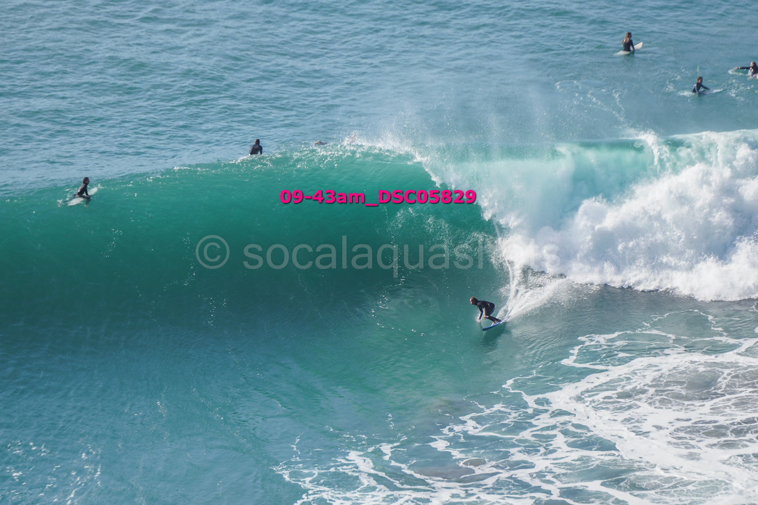 A person surfing on a large wave with several other surfers in the water nearby.