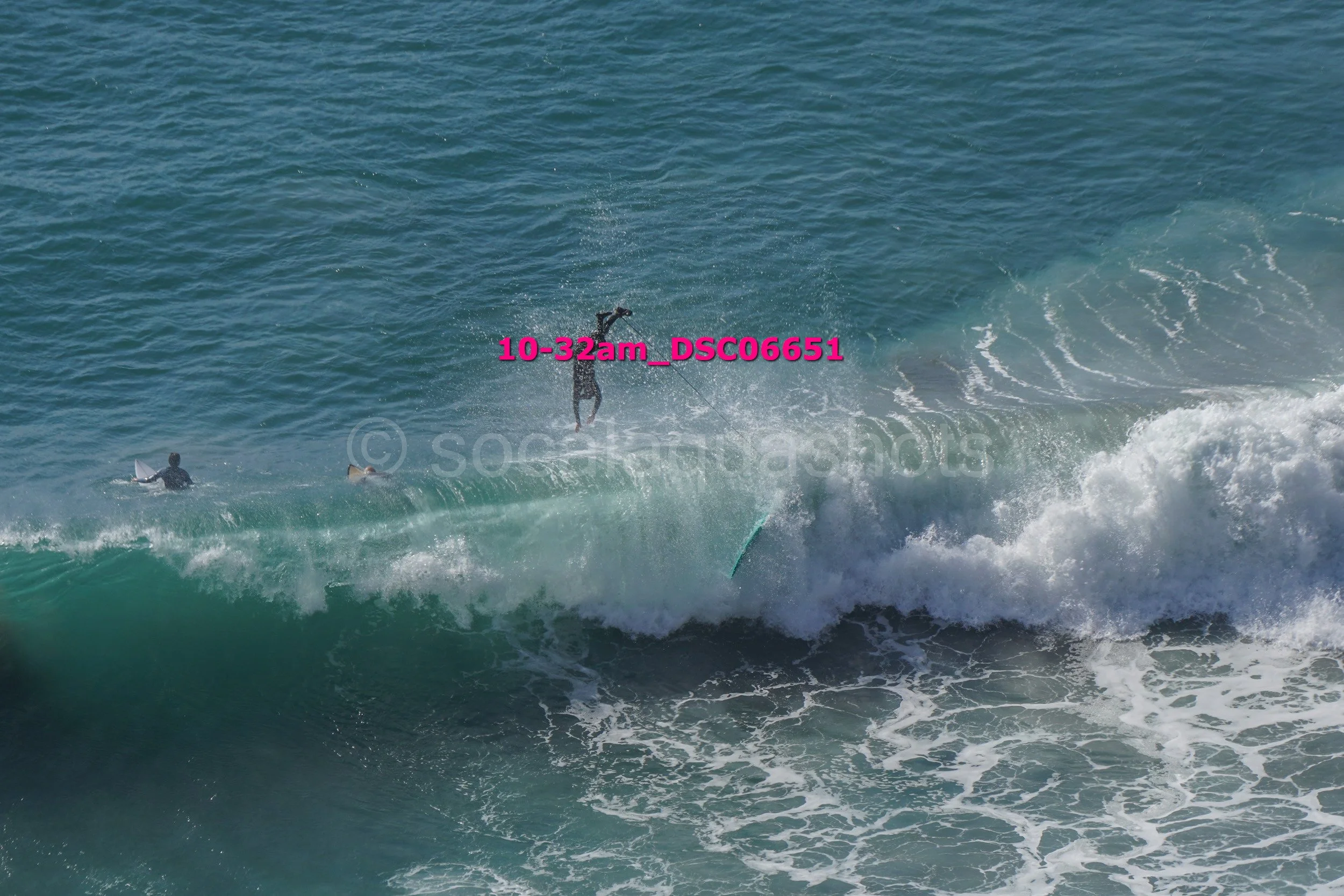 Surfer falling off a wave while two other surfers wait in the water.