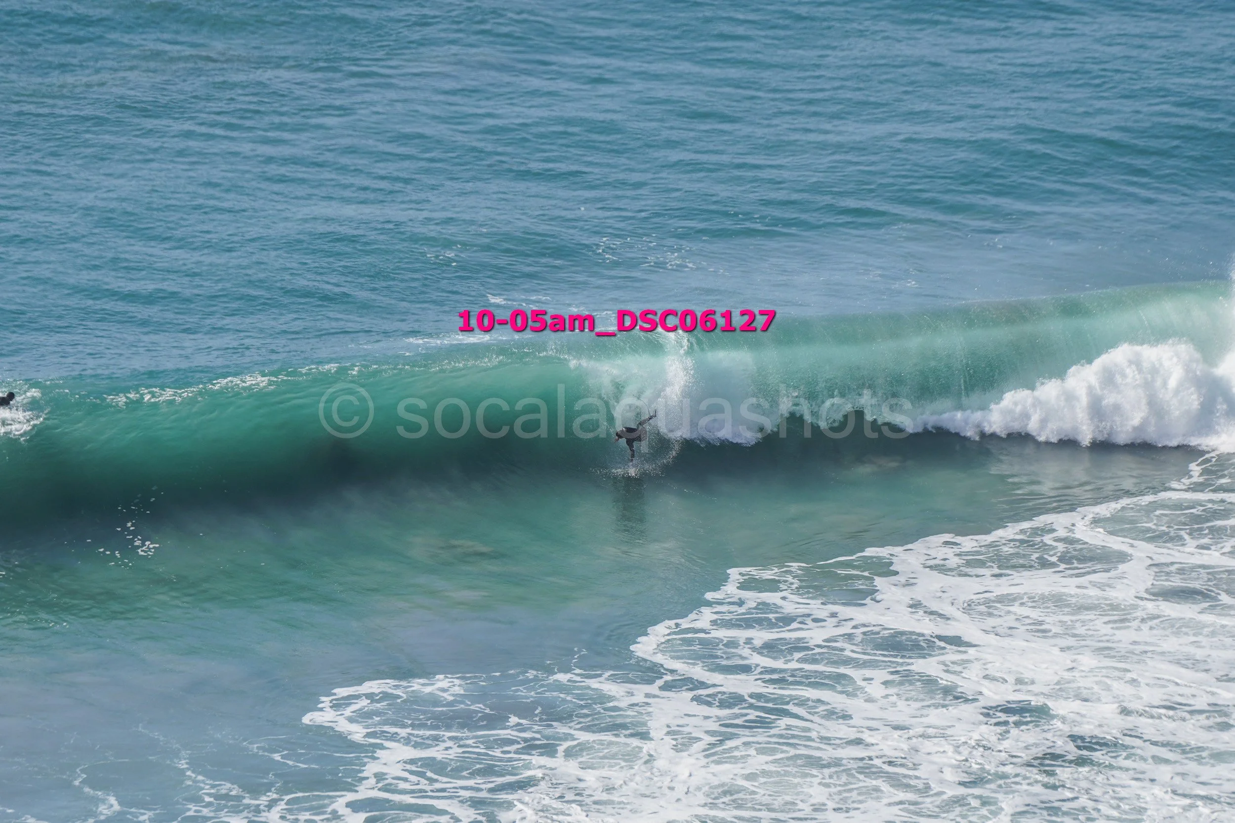 A person surfing on a large ocean wave with a clear blue sky.