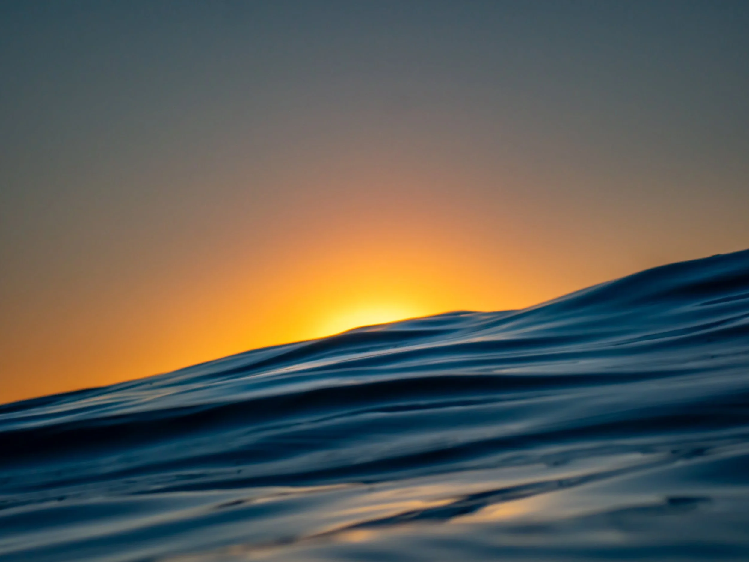 Close-up of ocean waves during sunset, with the sun setting behind the horizon in the background.