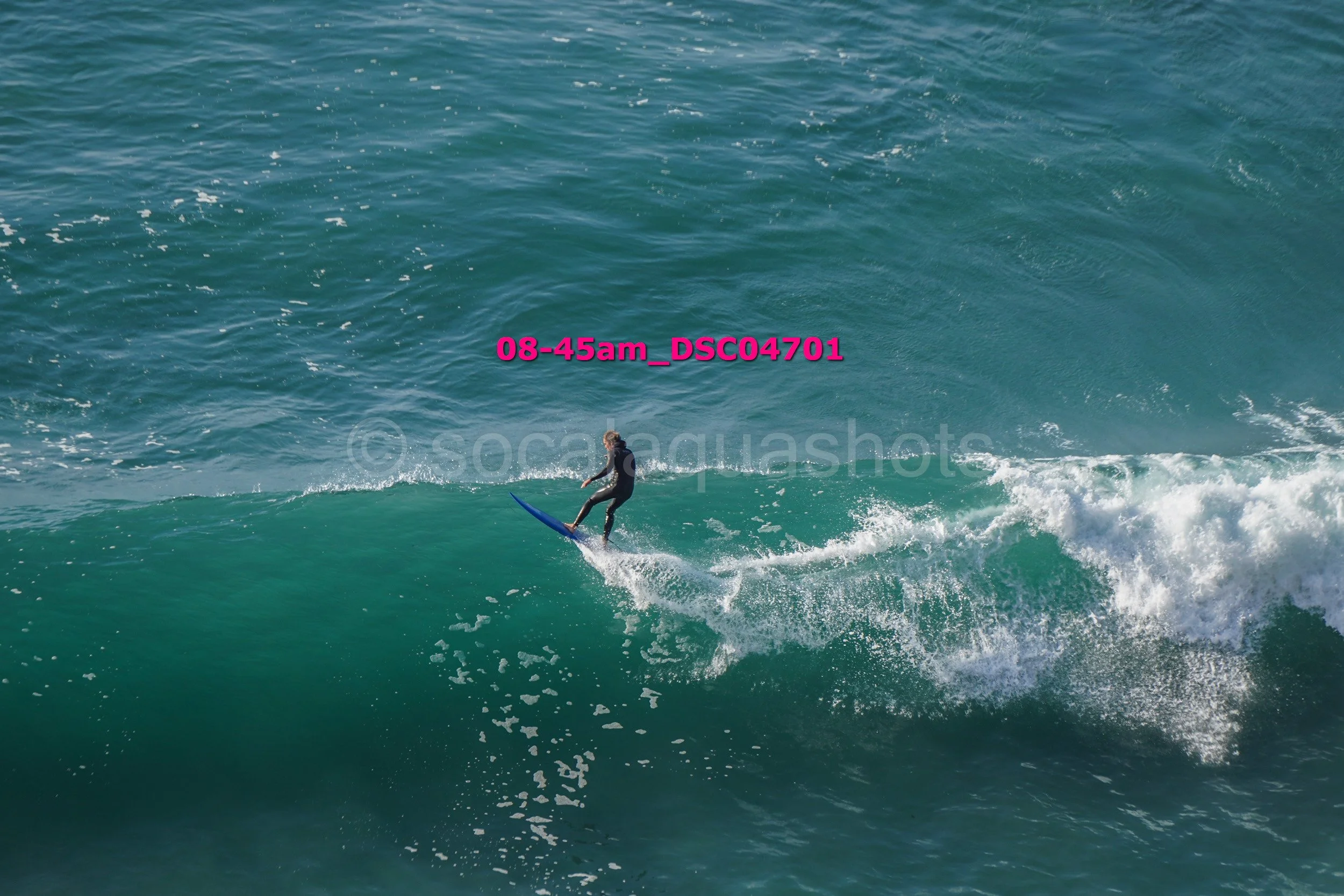A person surfing on a wave in the ocean, wearing a black wetsuit.