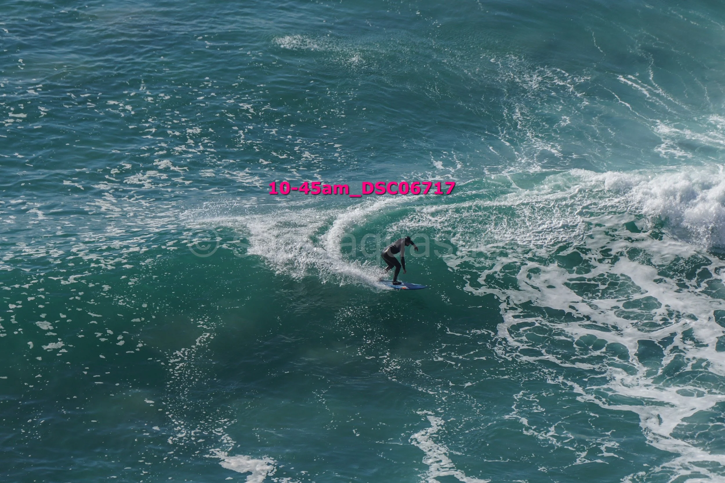 A person surfing on a wave in the ocean. The image has text overlay '10-45am_DSC0717' in pink.