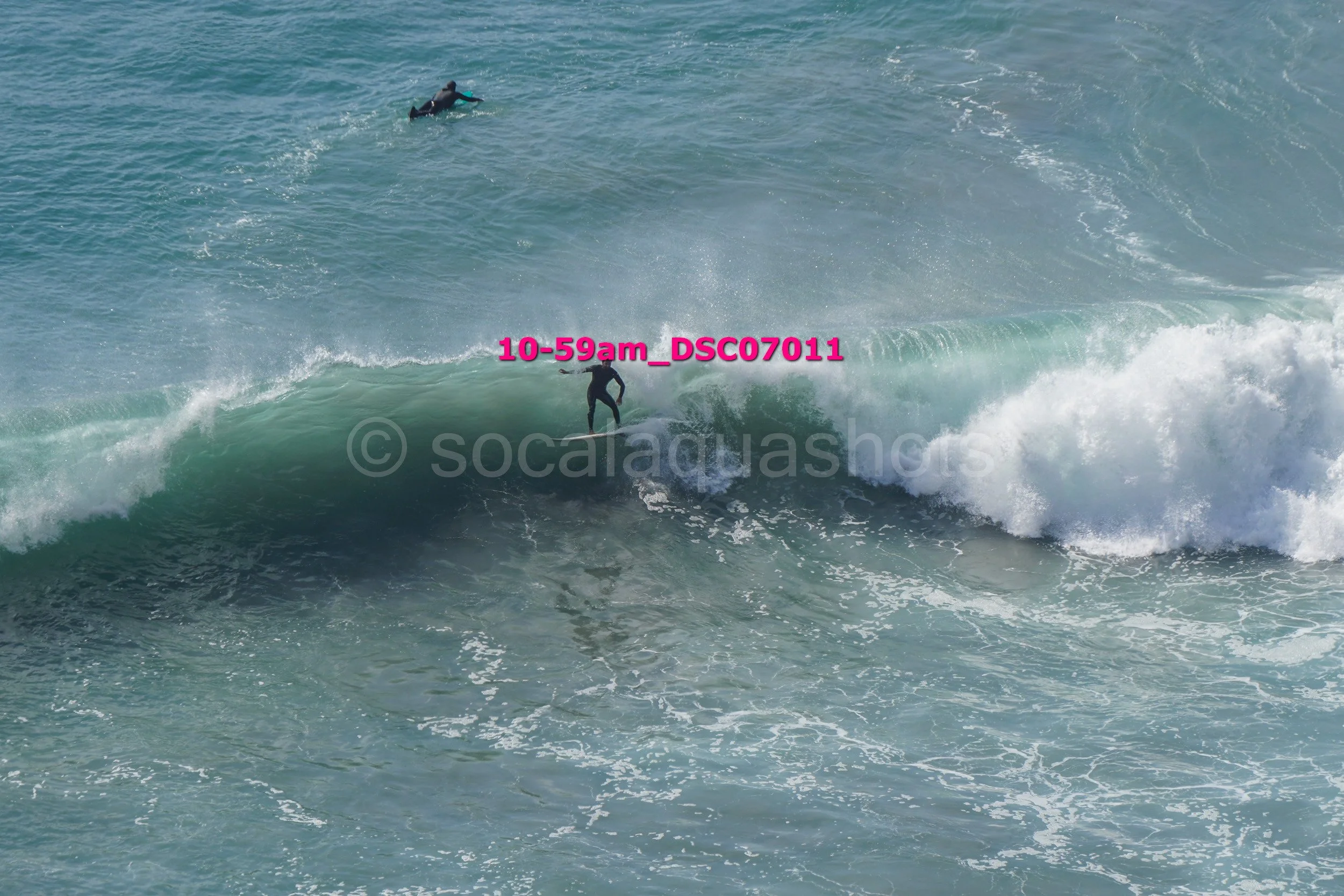 Surfer riding a wave with two other surfers swimming in the ocean in the background.