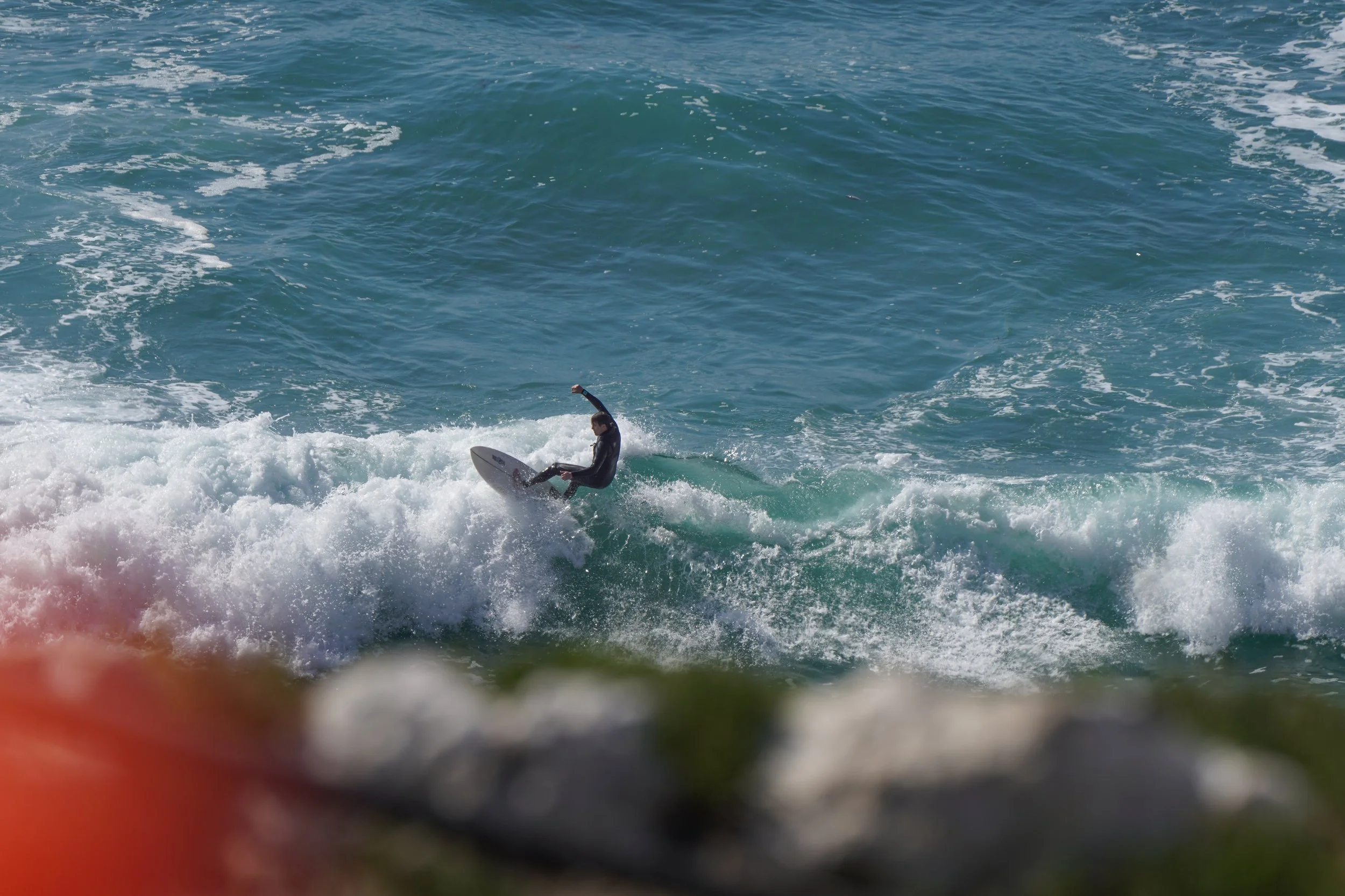 A person surfing on a wave in the ocean, wearing a wetsuit.