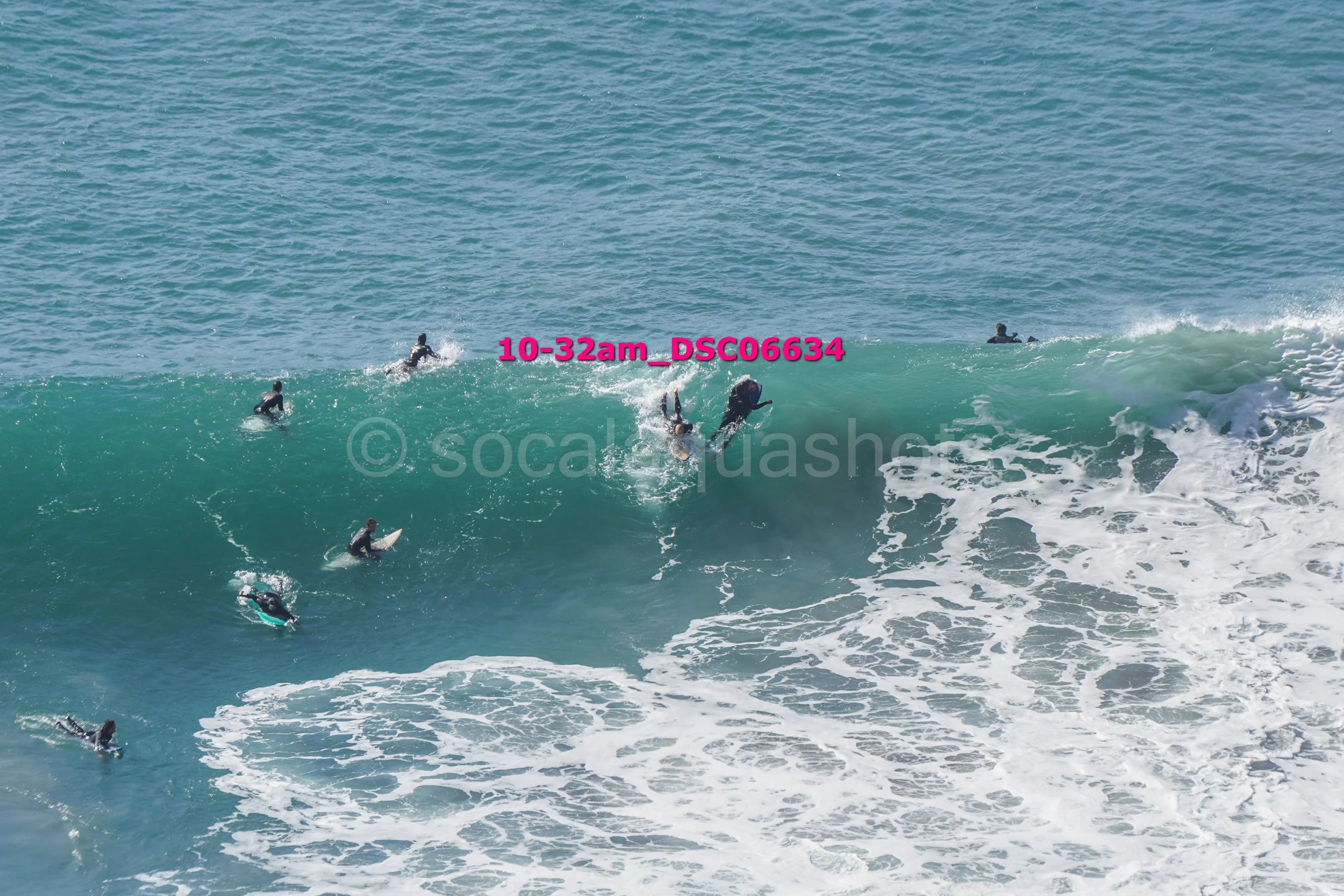 Multiple surfers riding a large wave in the ocean with clear blue water