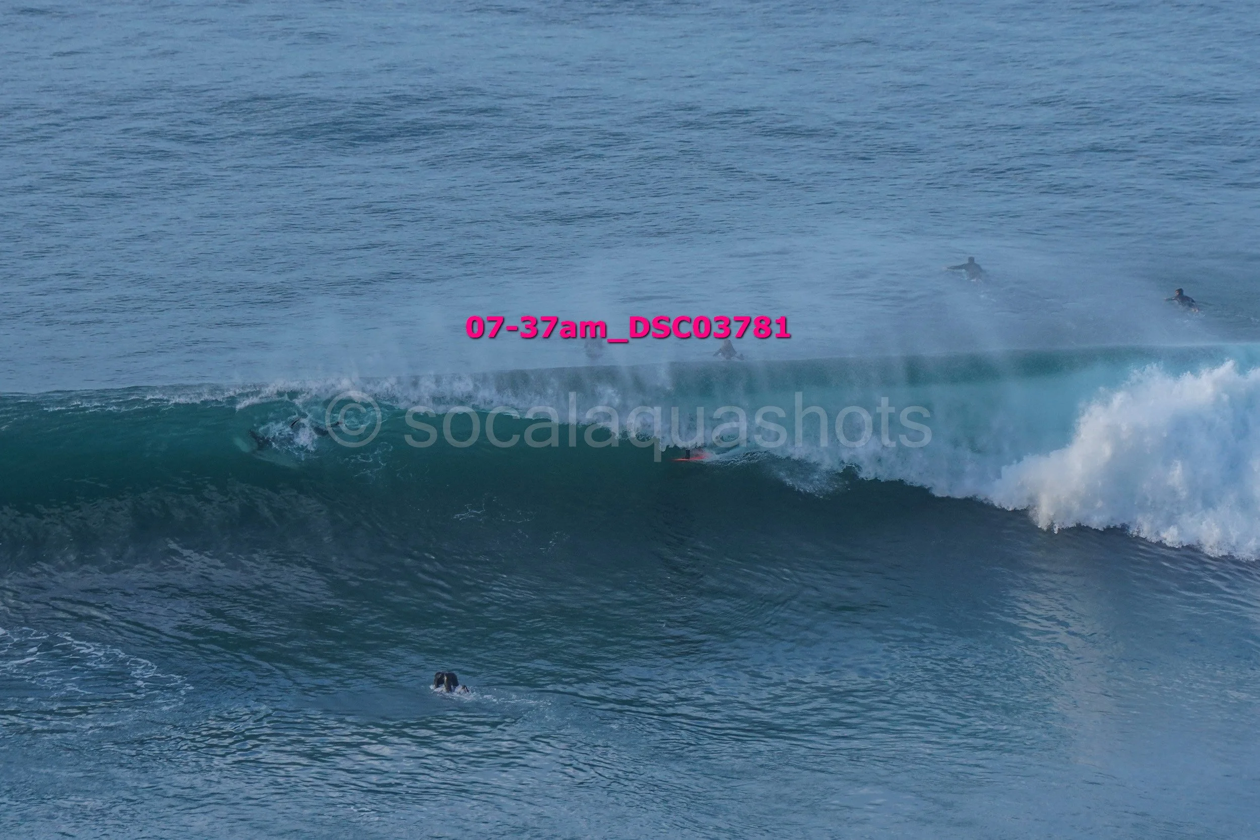 Surfers riding a large wave in the ocean with a swimmer in the foreground.