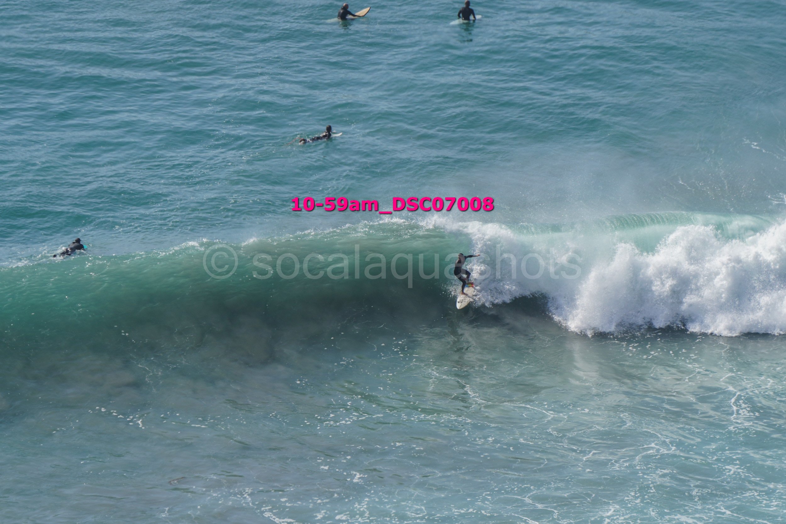 Surfer riding a wave with surfers in the distance in the ocean.