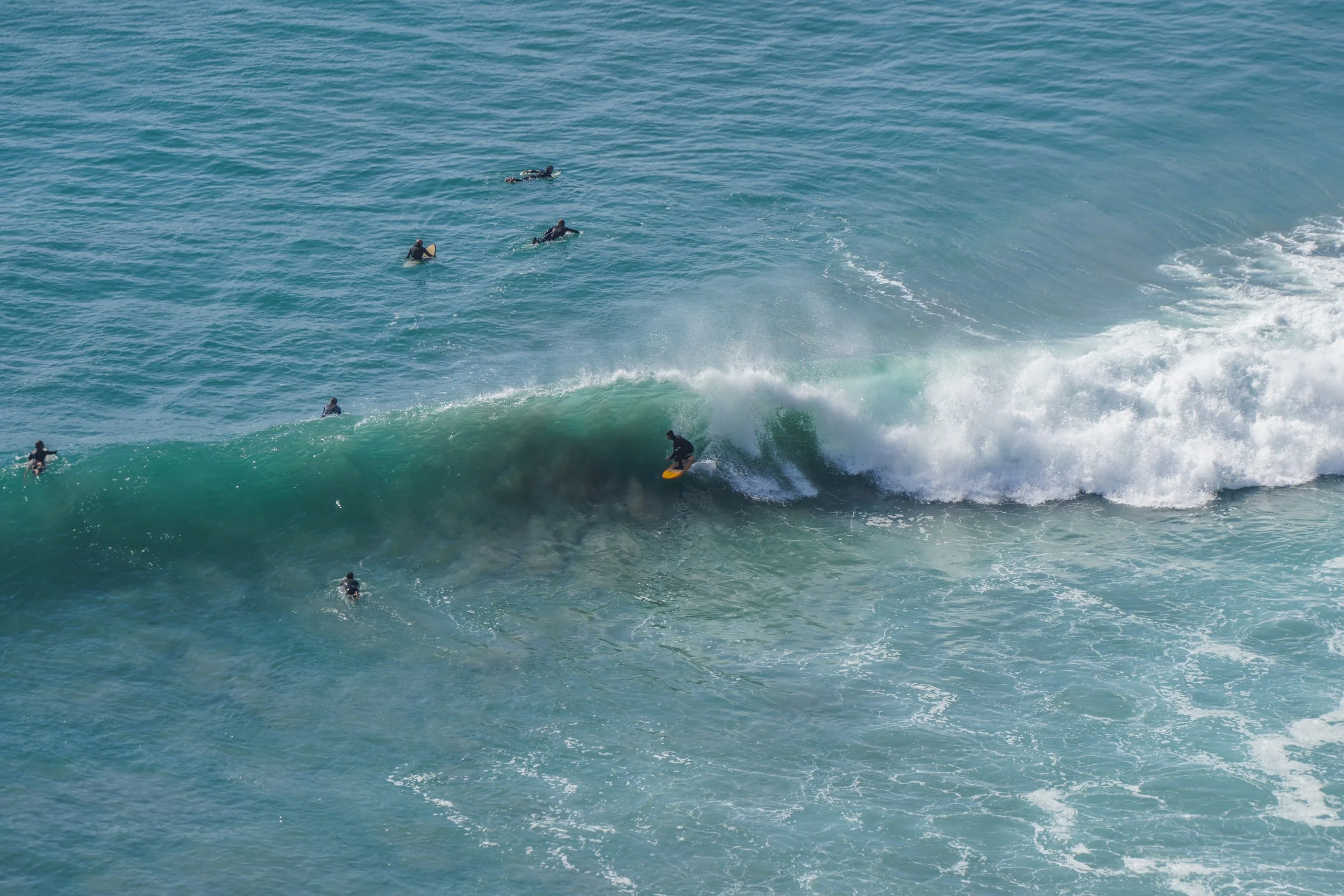 Surfer riding a wave near several surfers in the ocean.