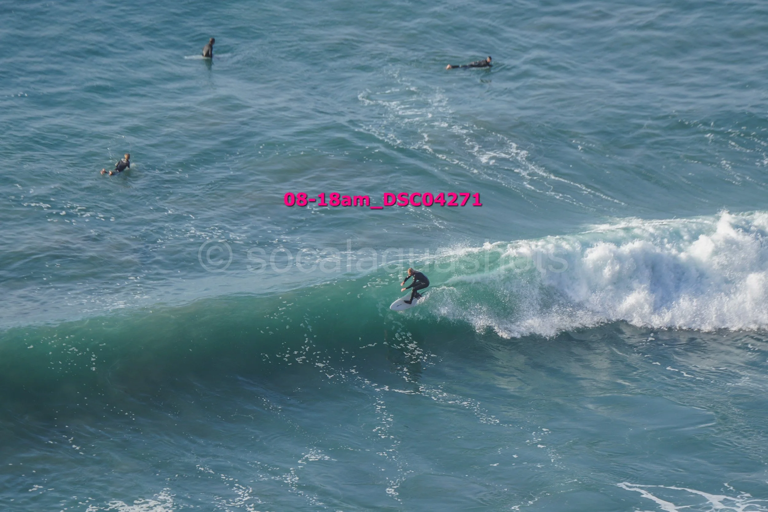A surfer riding a wave in the ocean with four other surfers floating nearby.