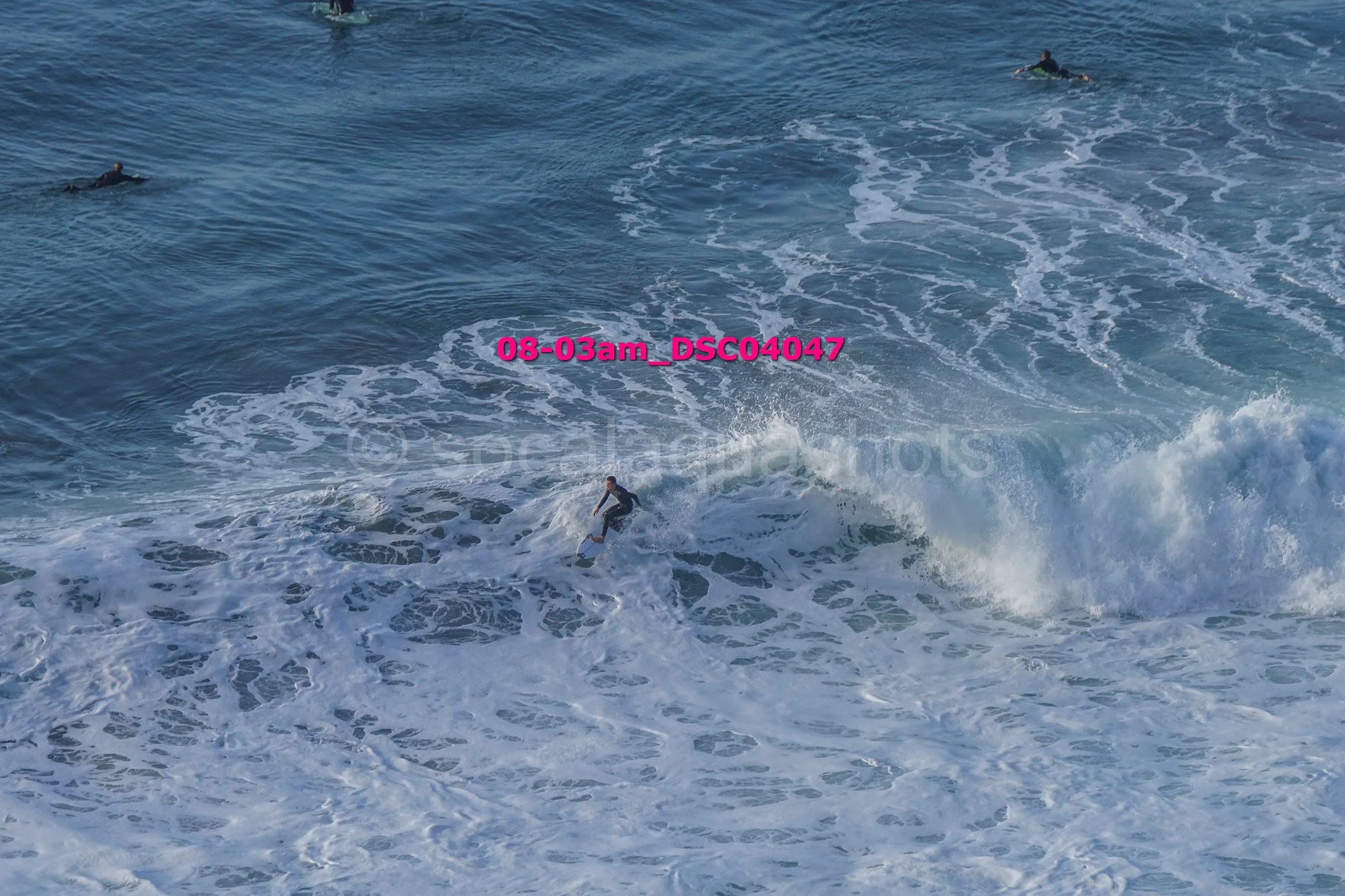 Surfer riding a wave in the ocean with two other surfers in the background