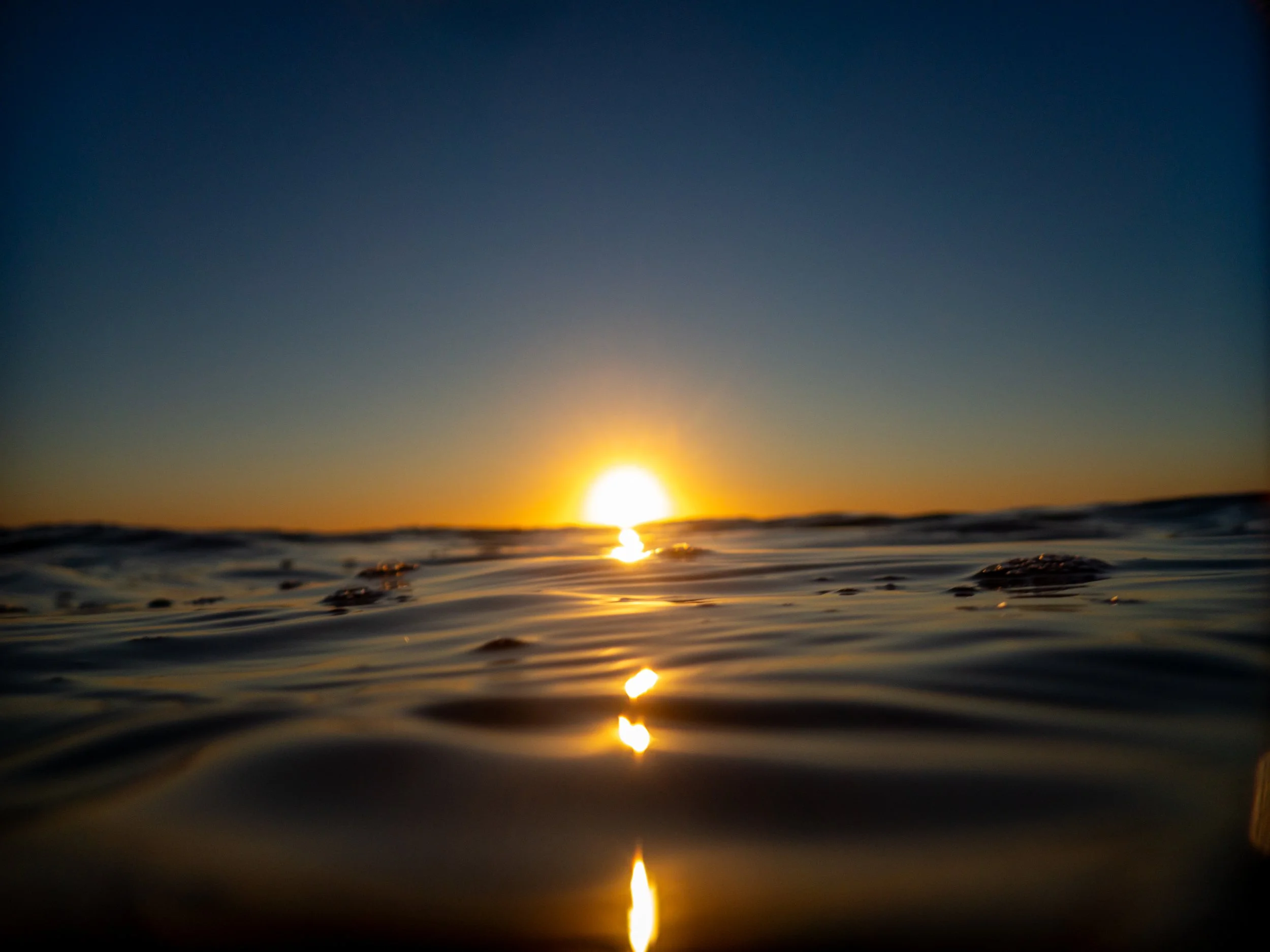 Sunset over the ocean with waves and the sun's reflection on the water.