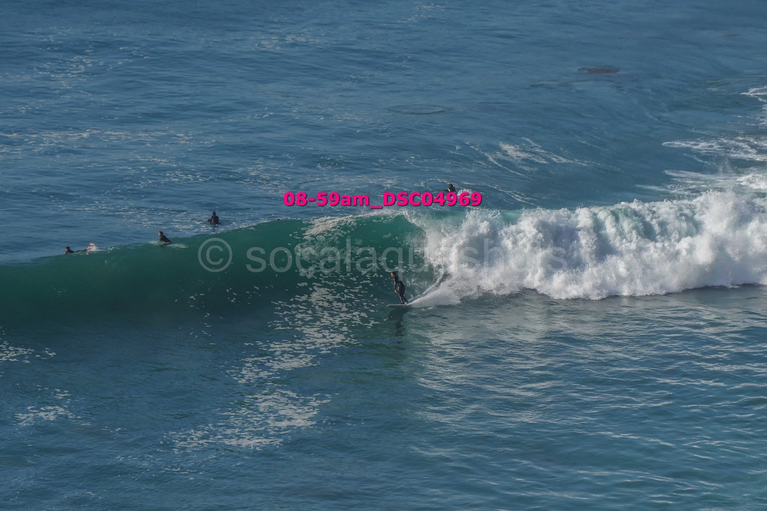 Surfer riding a wave in the ocean with several other surfers on the water nearby.