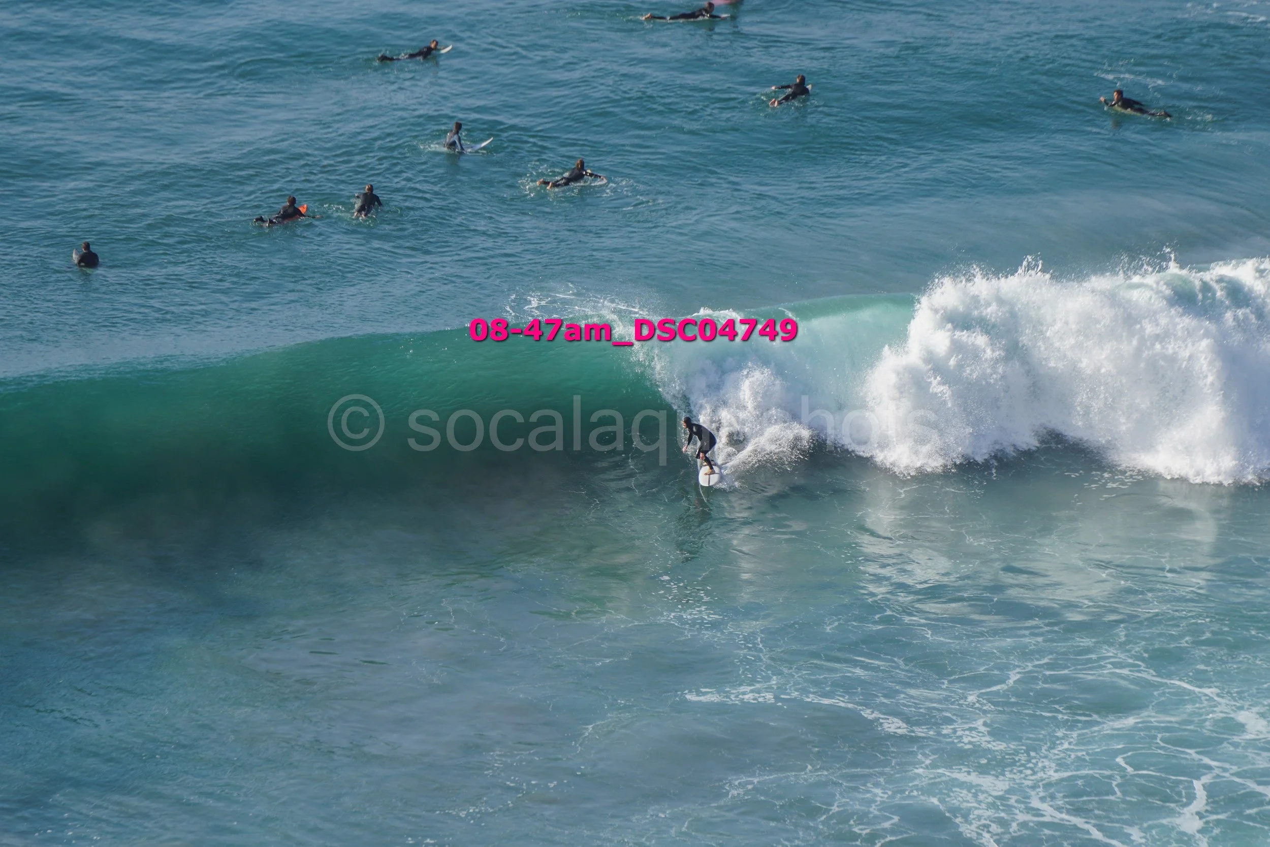 Surfer riding a large wave with several people surfing in the background in the ocean.