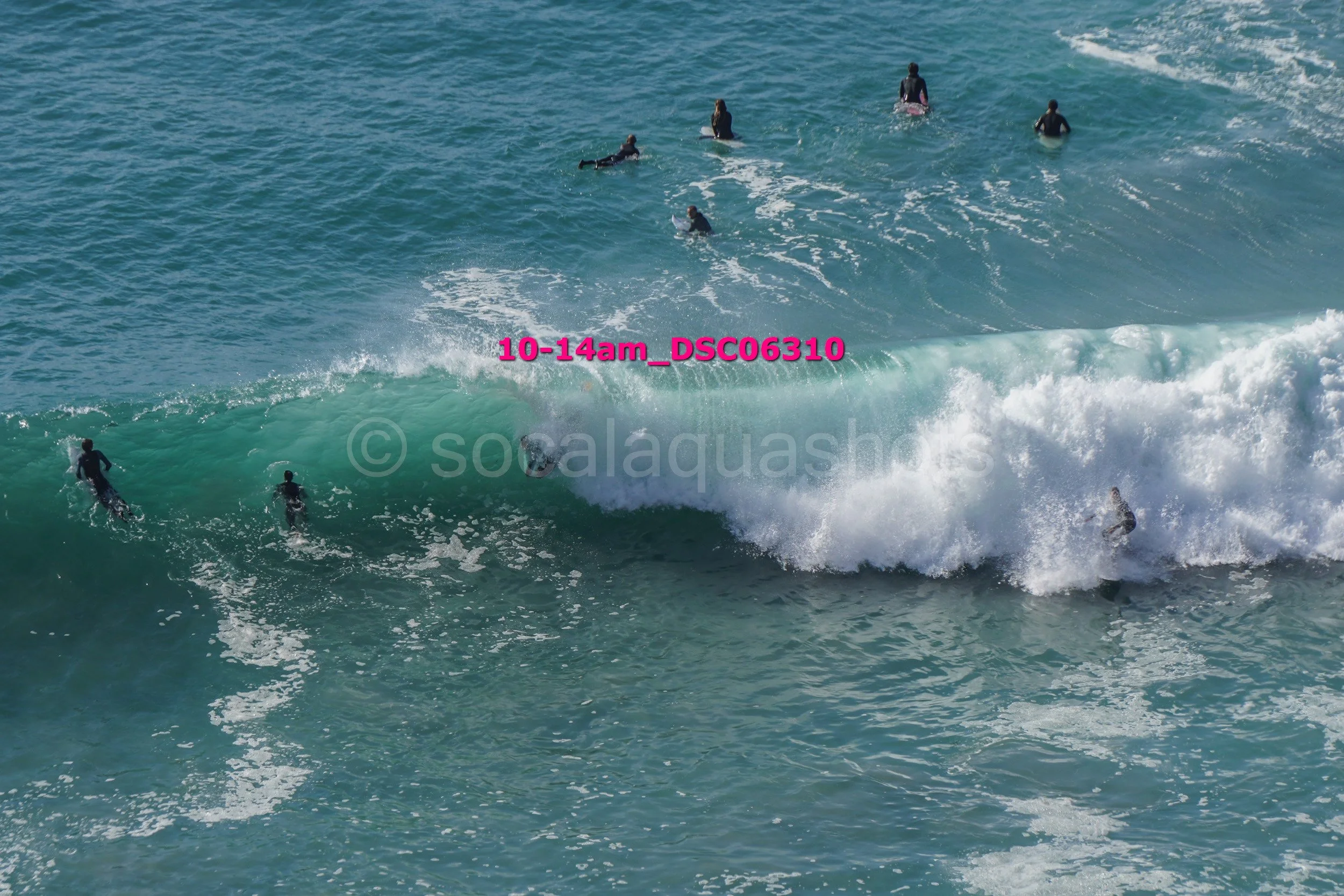 Several surfers in wetsuits enjoying waves at the beach, with some catching a wave and others paddling.