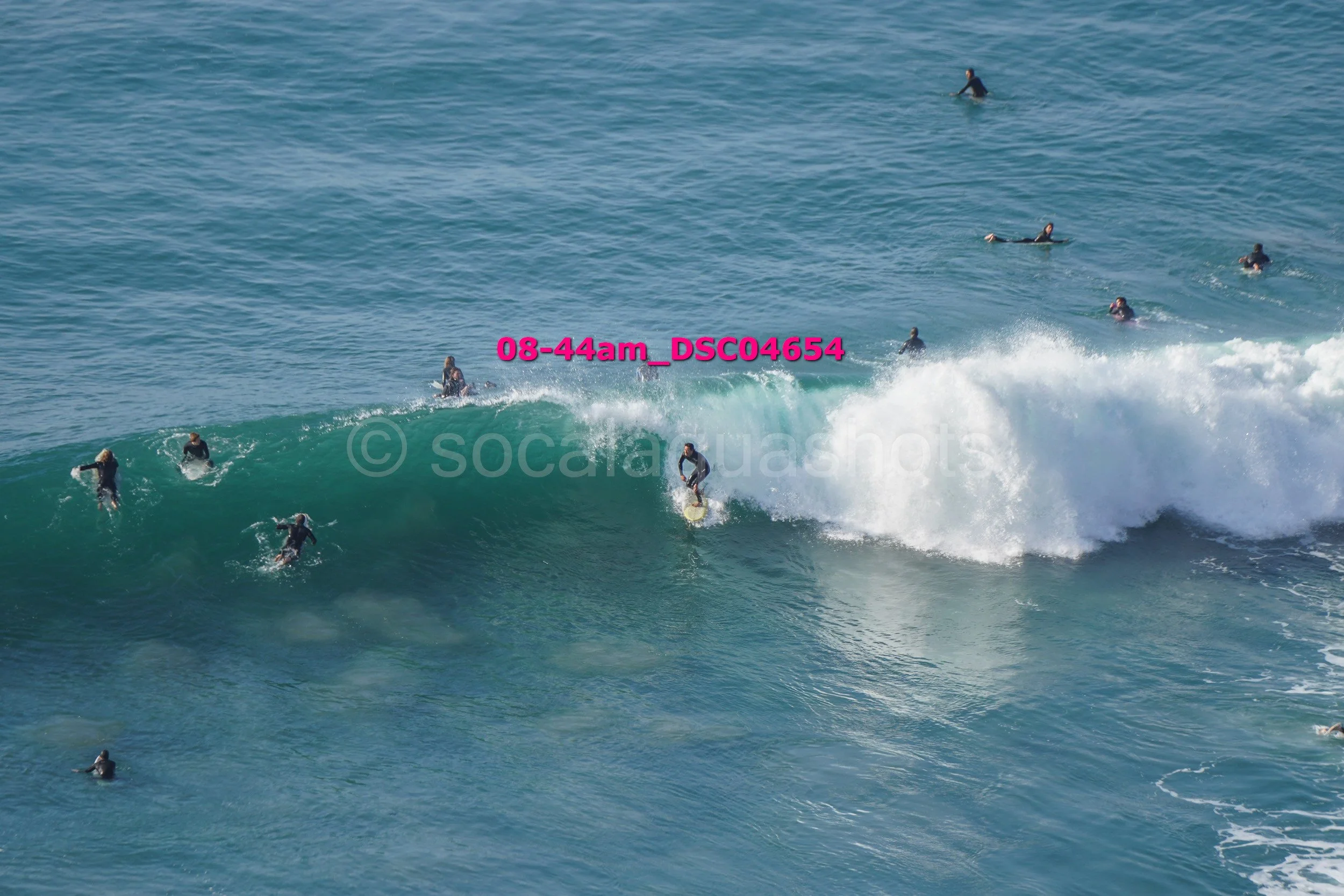 Surfers in wetsuits riding and waiting for waves in the ocean.