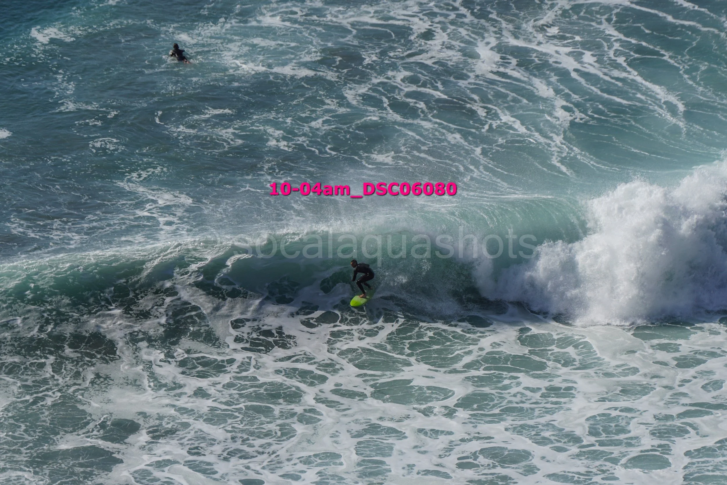 Surfer riding a wave in the ocean, with another surfer visible in the water nearby.