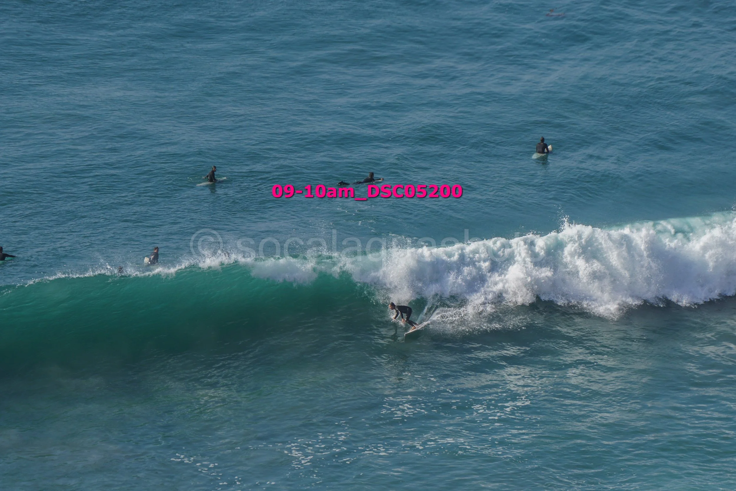 A surfer riding a wave in the ocean, with several other surfers on surfboards in the water in the background.