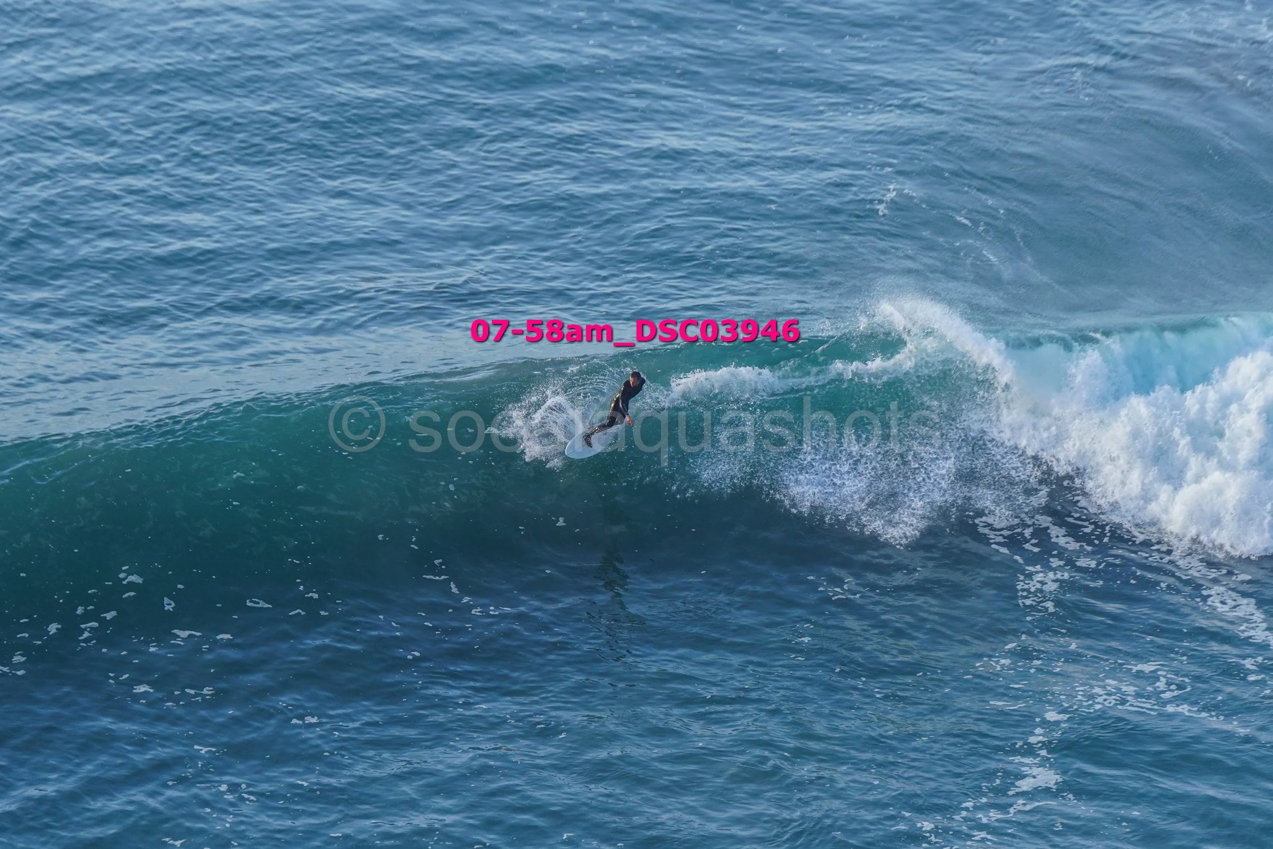 A person surfing on a large wave in the ocean, with the sky and water visible in the background.