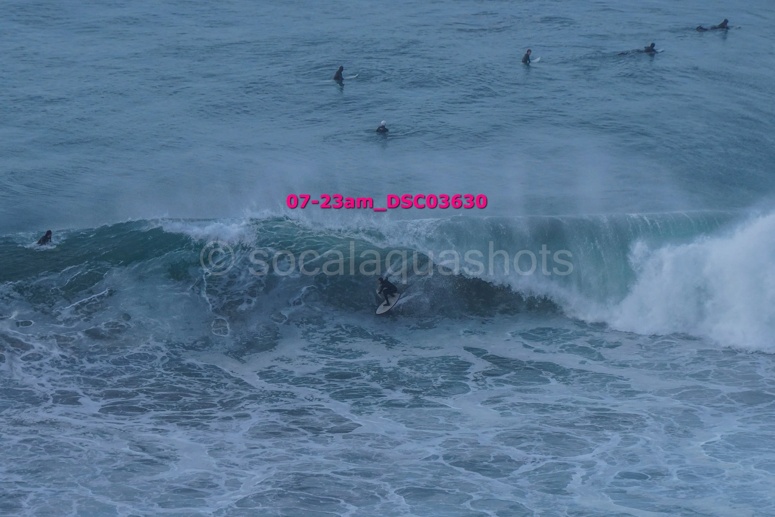 Surfer riding a large wave with several surfers in the water in the background.