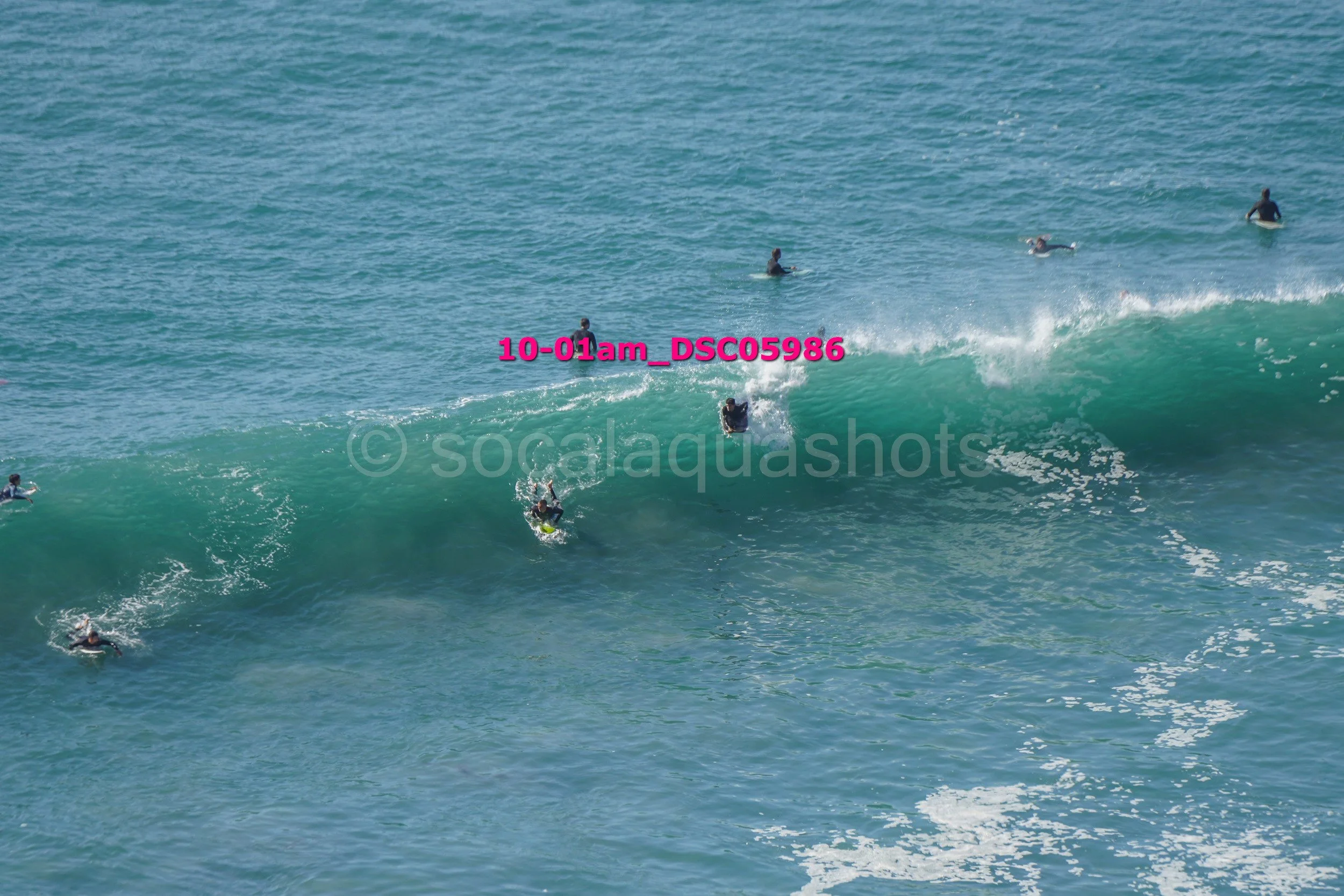 Several surfers and bodyboarders riding and waiting for waves in the ocean, with one person actively surfing a large wave.