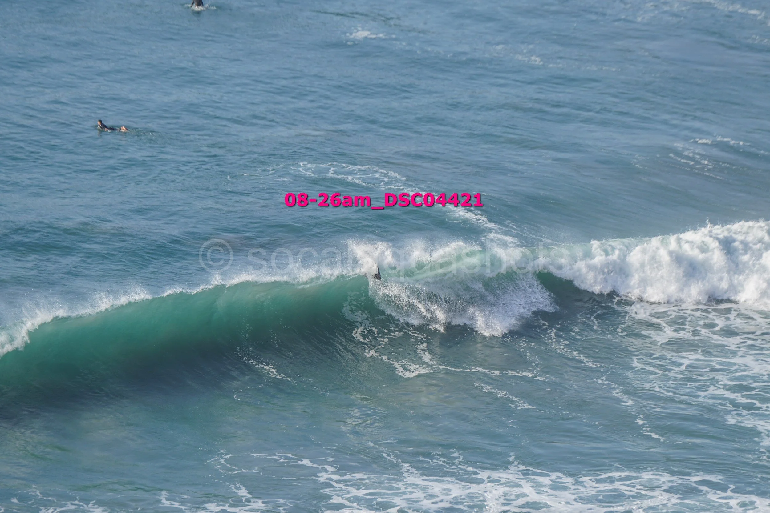 A person surfing a wave in the ocean with another person floating in the water nearby.