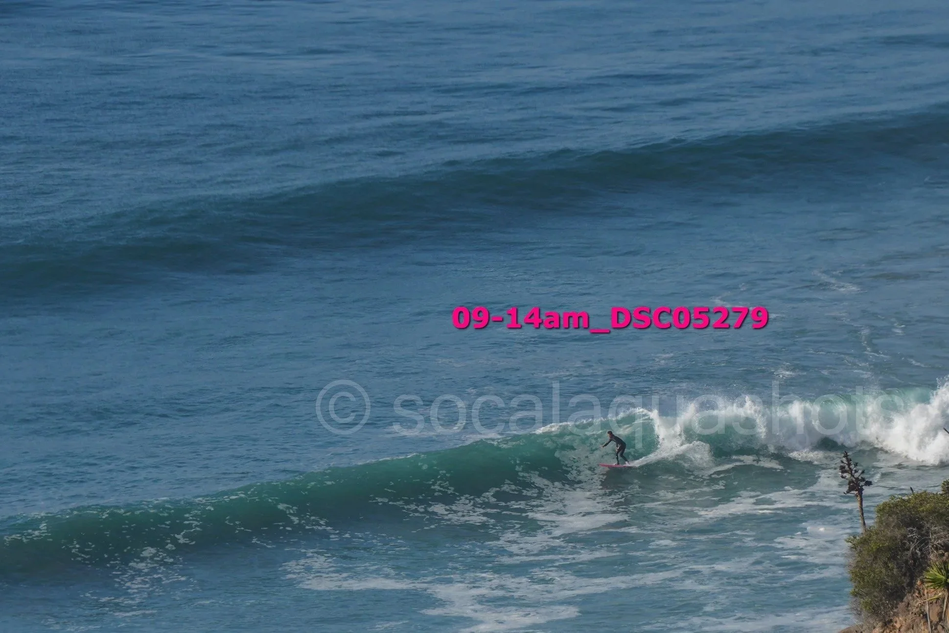 A person surfing on a wave in the ocean near a rocky shoreline with some vegetation.