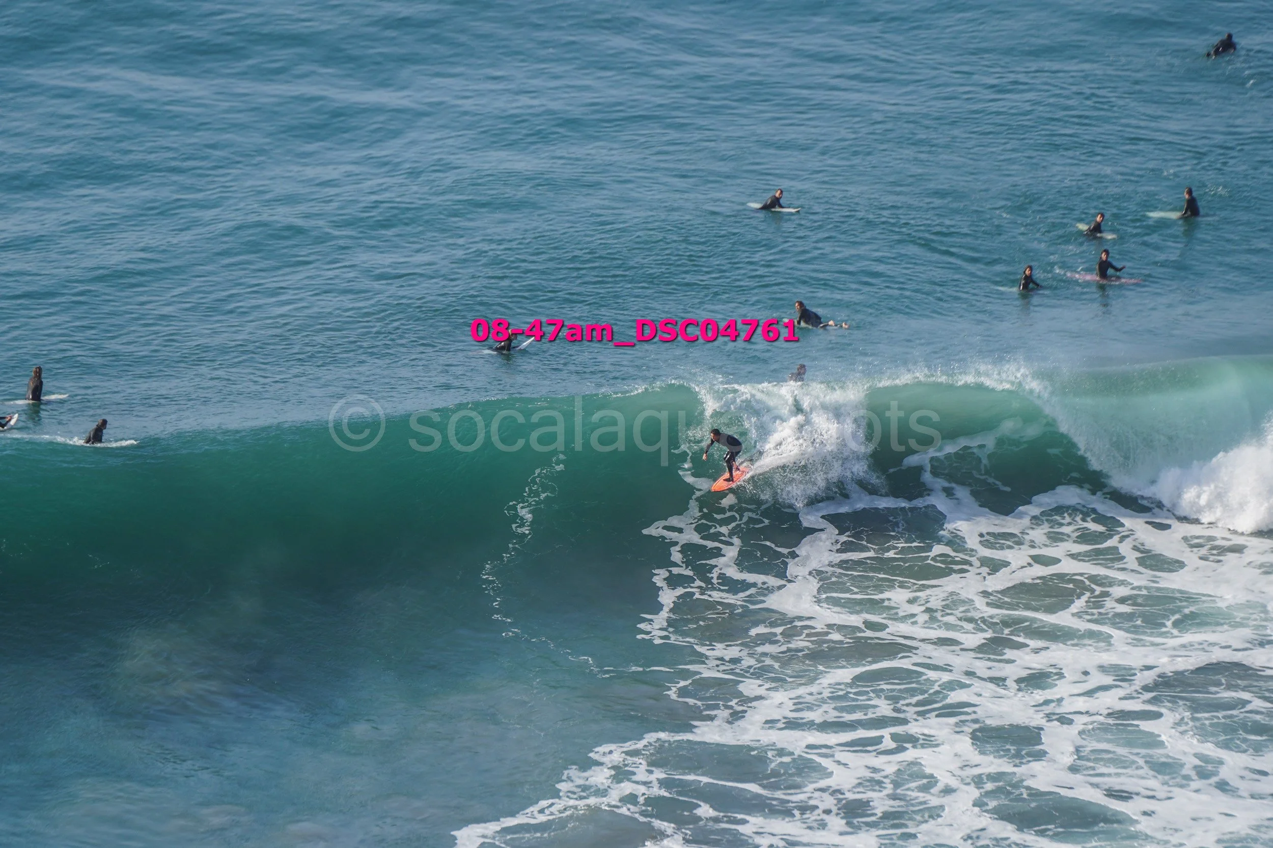 Surfer riding a wave while multiple surfers wait in the water in the background.