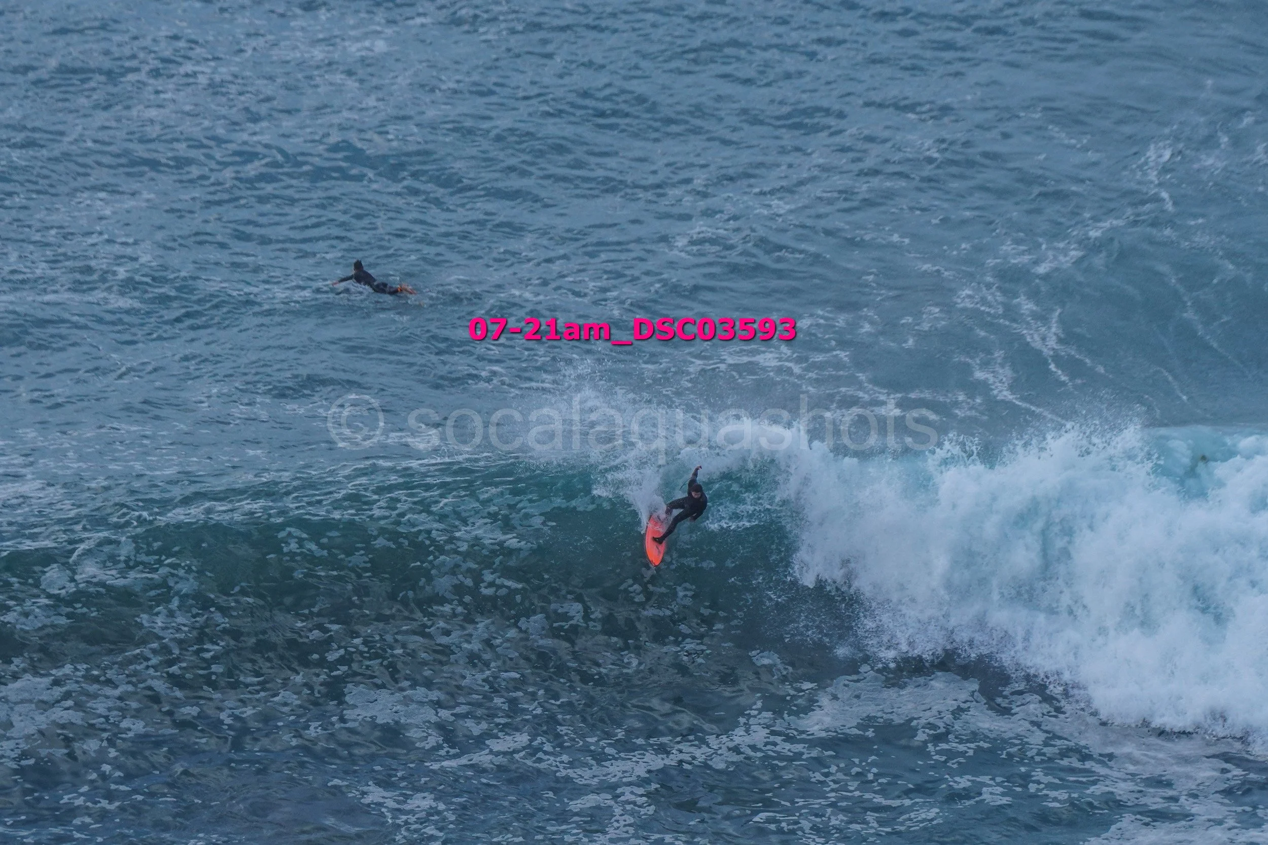 A person surfing on a wave with another person swimming in the background in the ocean.