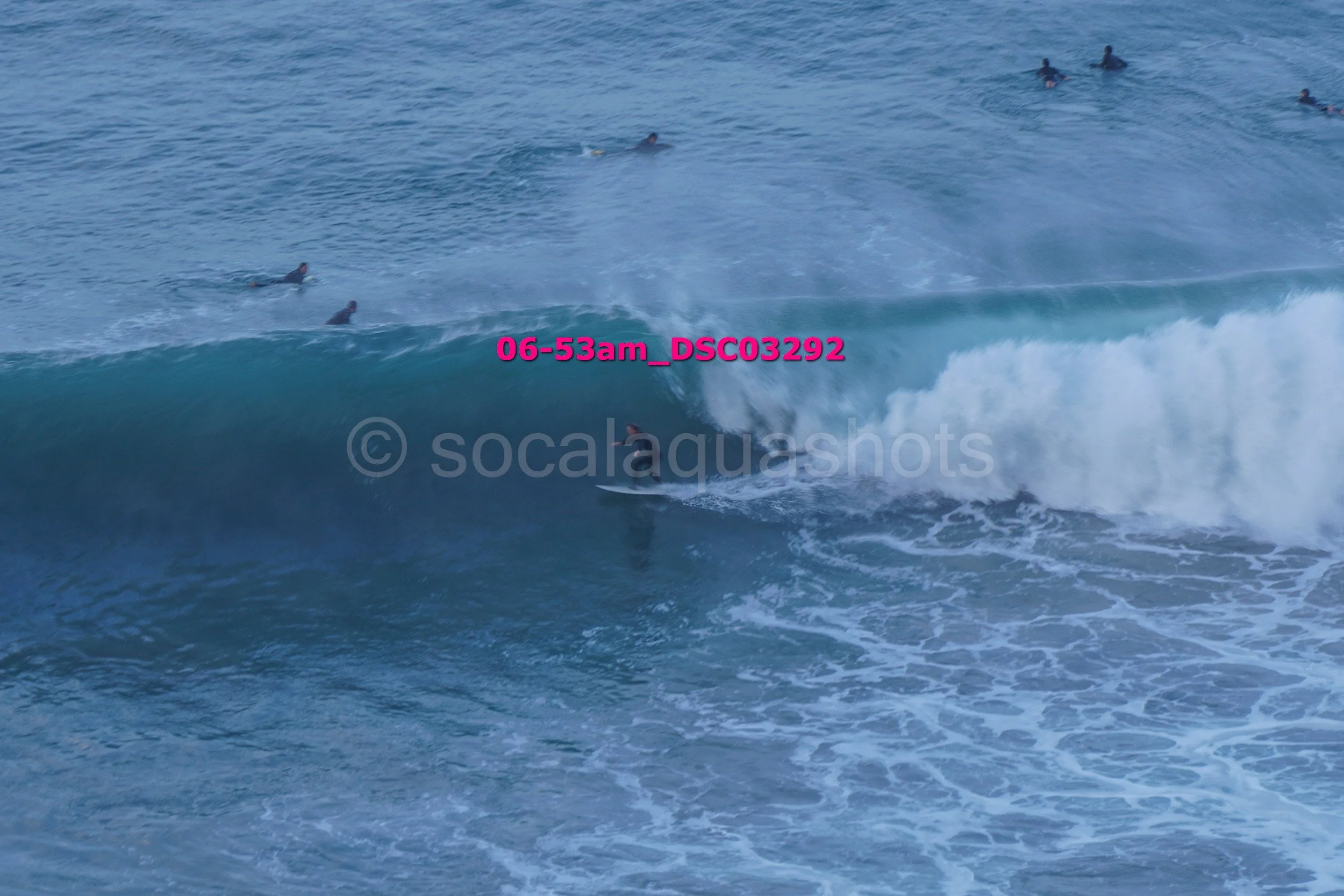 Surfer riding a large wave while multiple surfers wait in the water in the background.