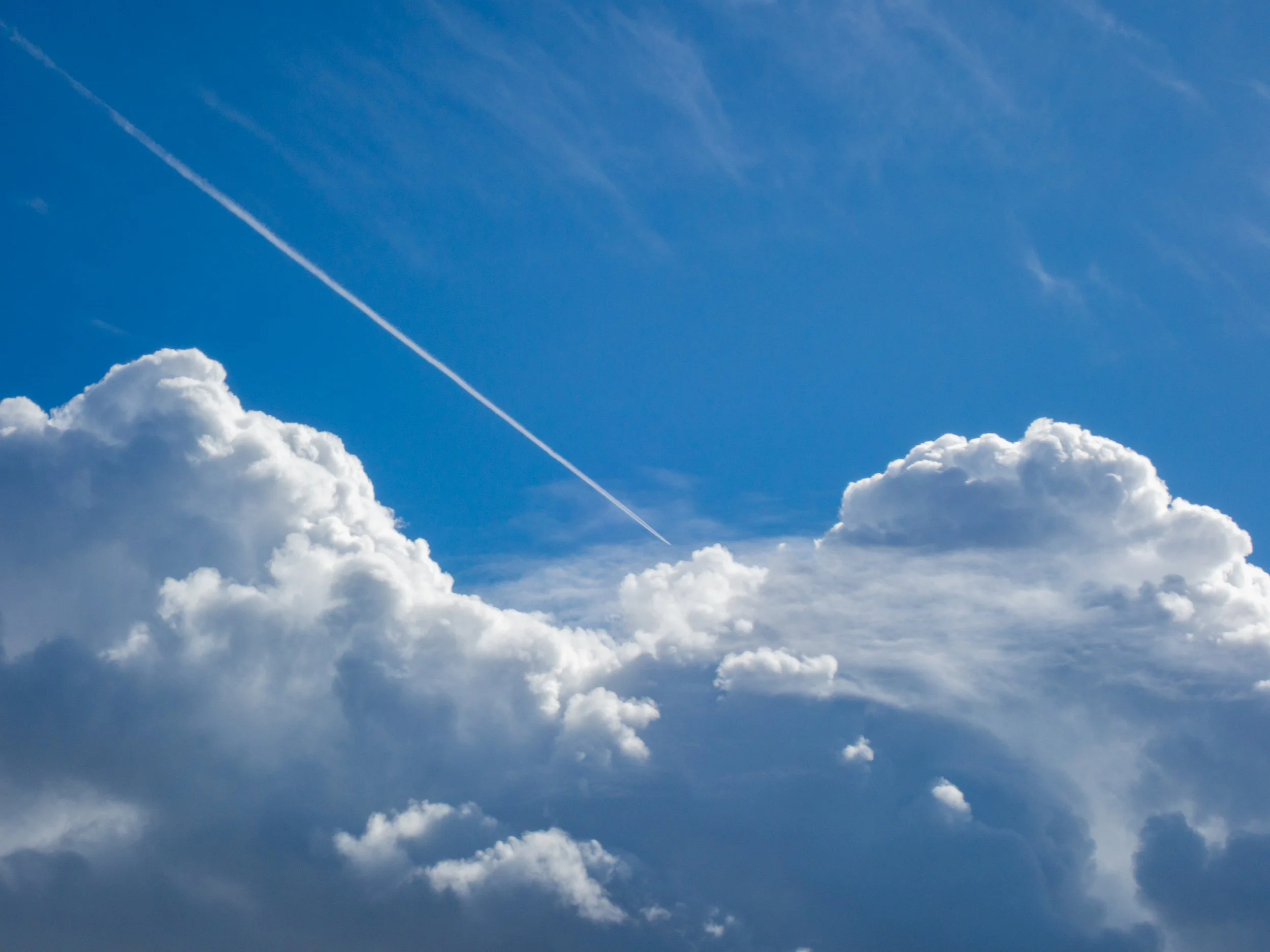 Blue sky with large white fluffy clouds and a contrail.