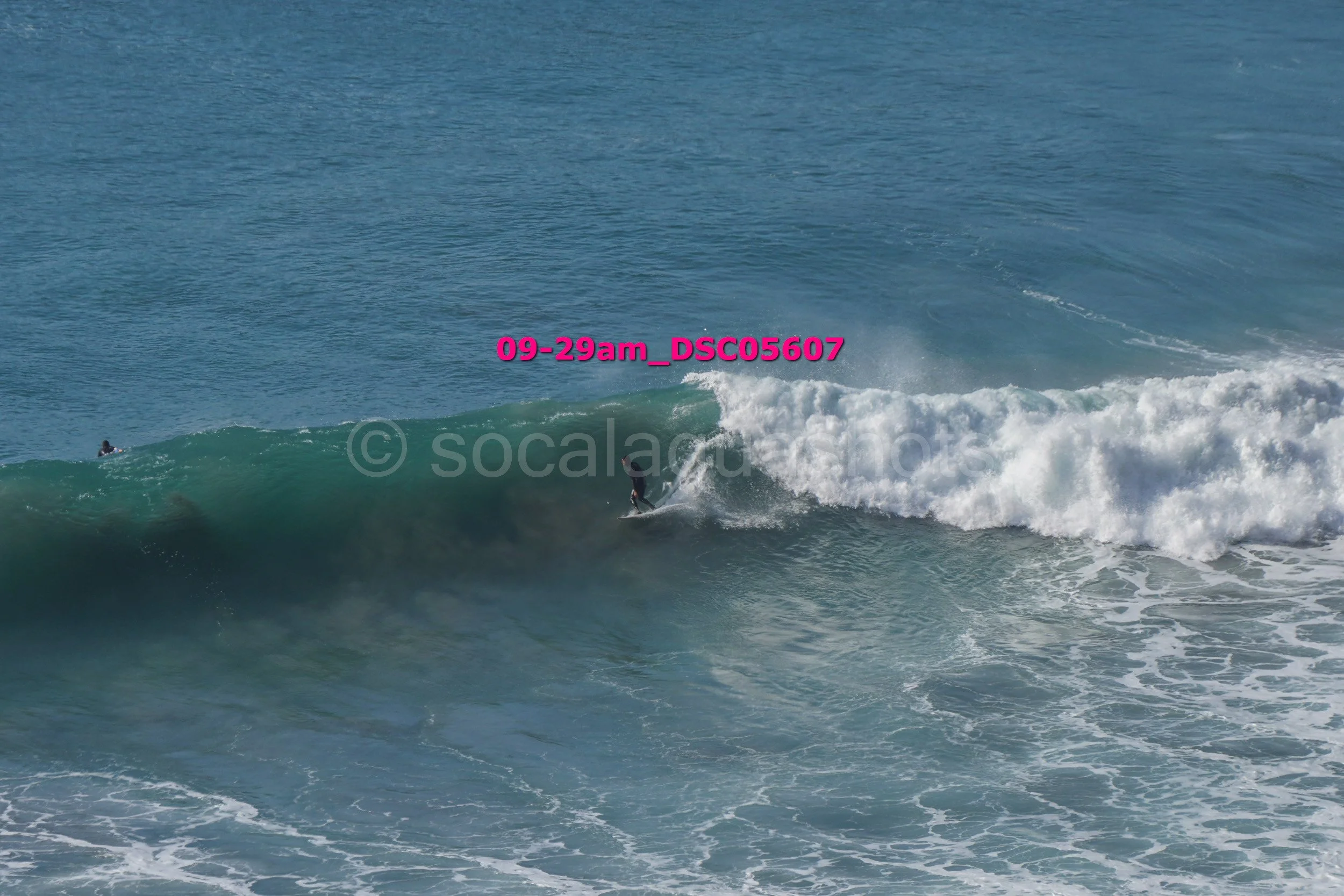 A surfer riding a large wave in the ocean with another person floating in the water nearby.