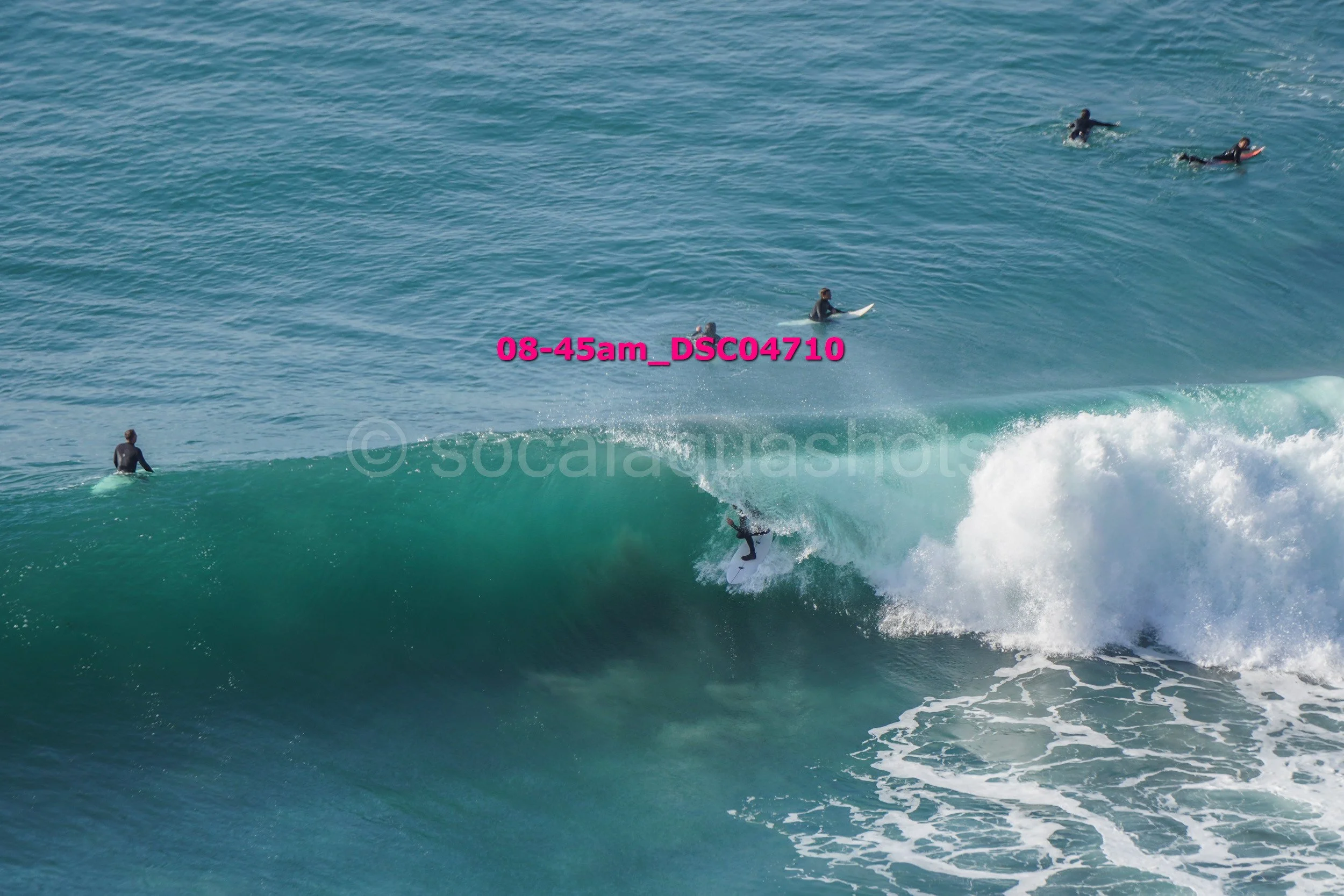 Surfer riding a wave with four other surfers in the water watching or waiting behind.