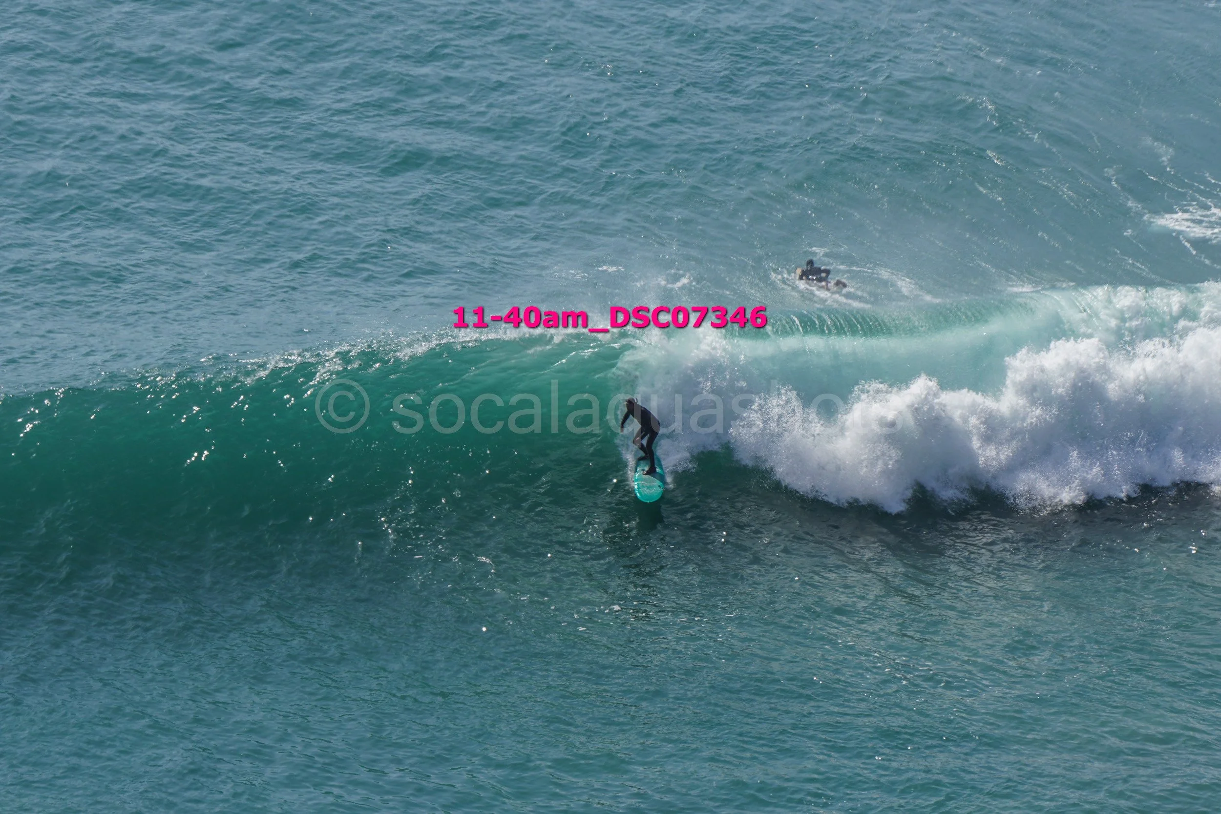 A person surfing a wave in the ocean, with another person in the background on a surfboard.