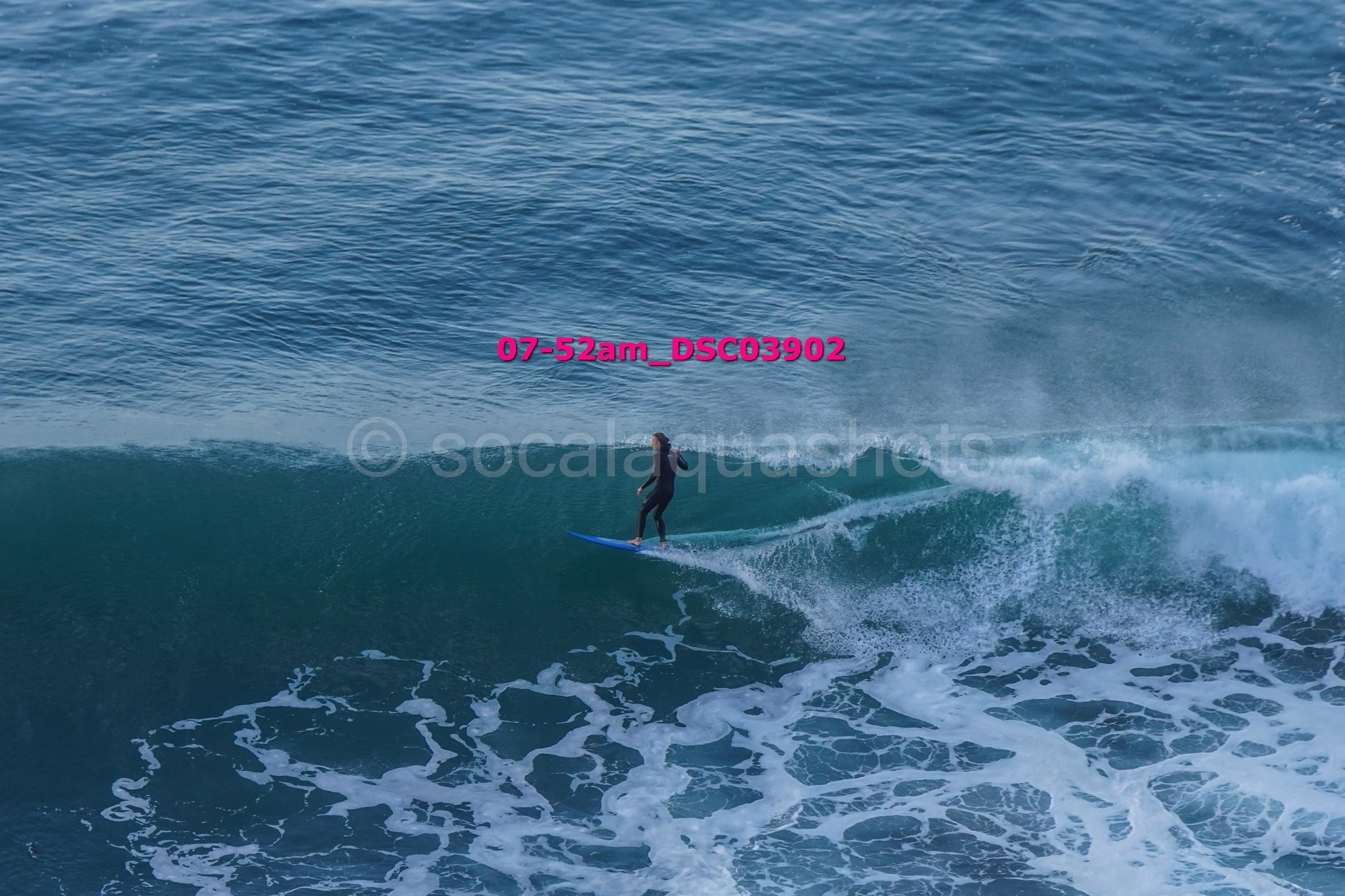 A person surfing on a blue surfboard on a wave in the ocean, with water splashing around.