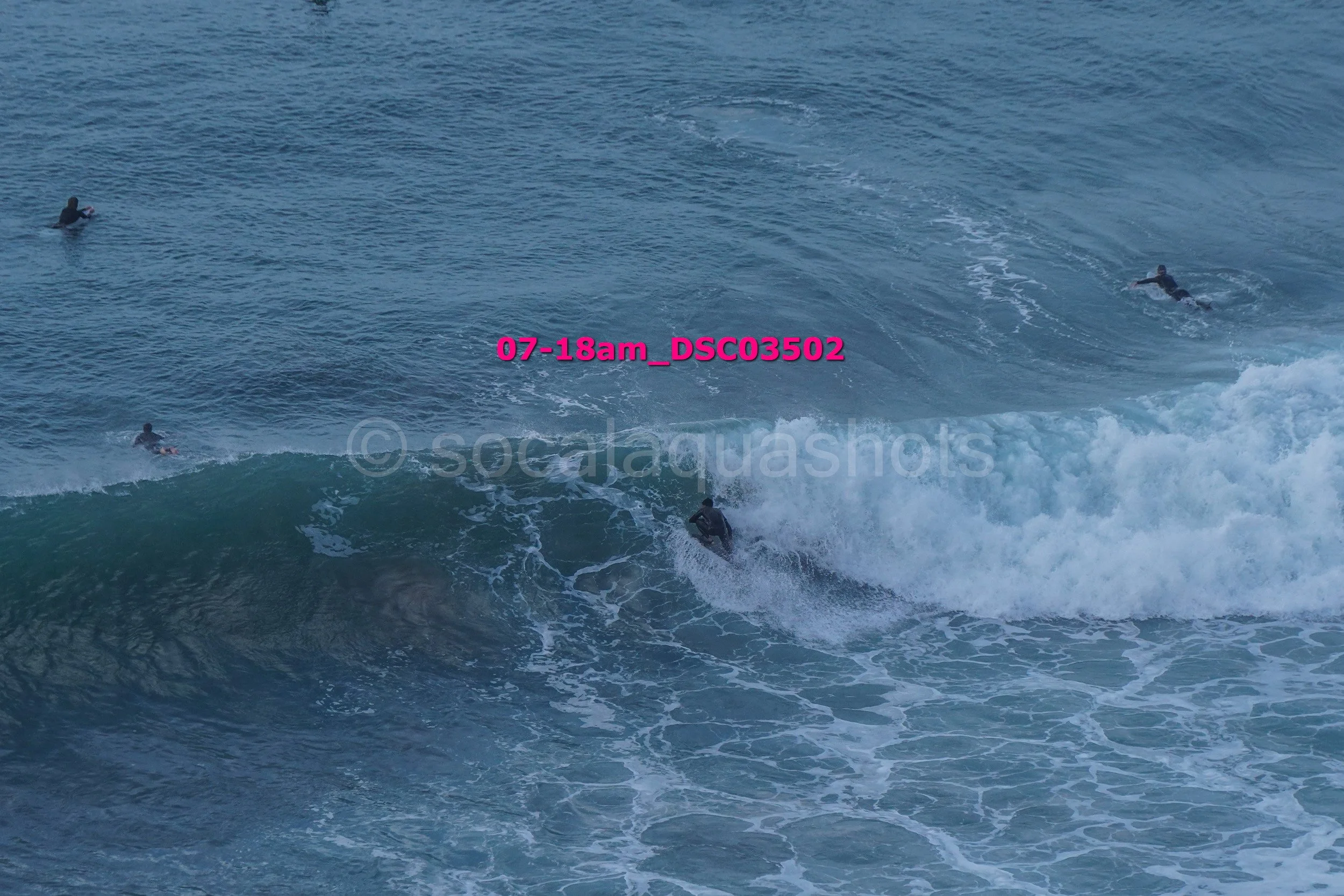 Surfers riding and waiting on ocean waves during daylight with clear sky.