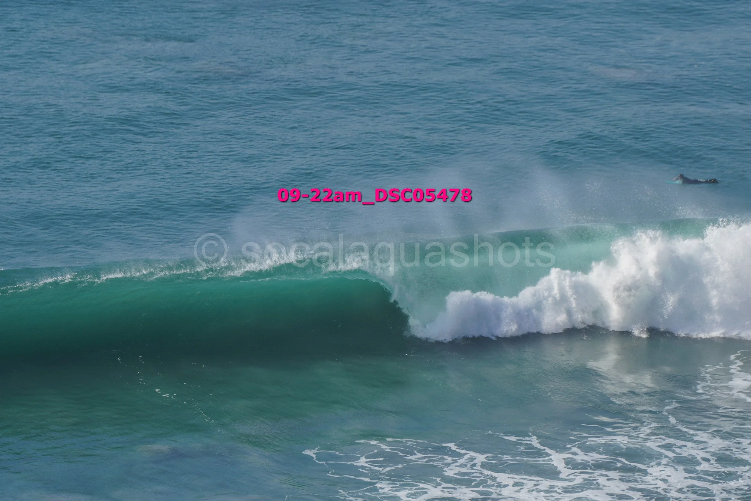 Image of ocean waves with a surfer in the distance, some waves crashing close to the shore, and water spraying on the wave crest.