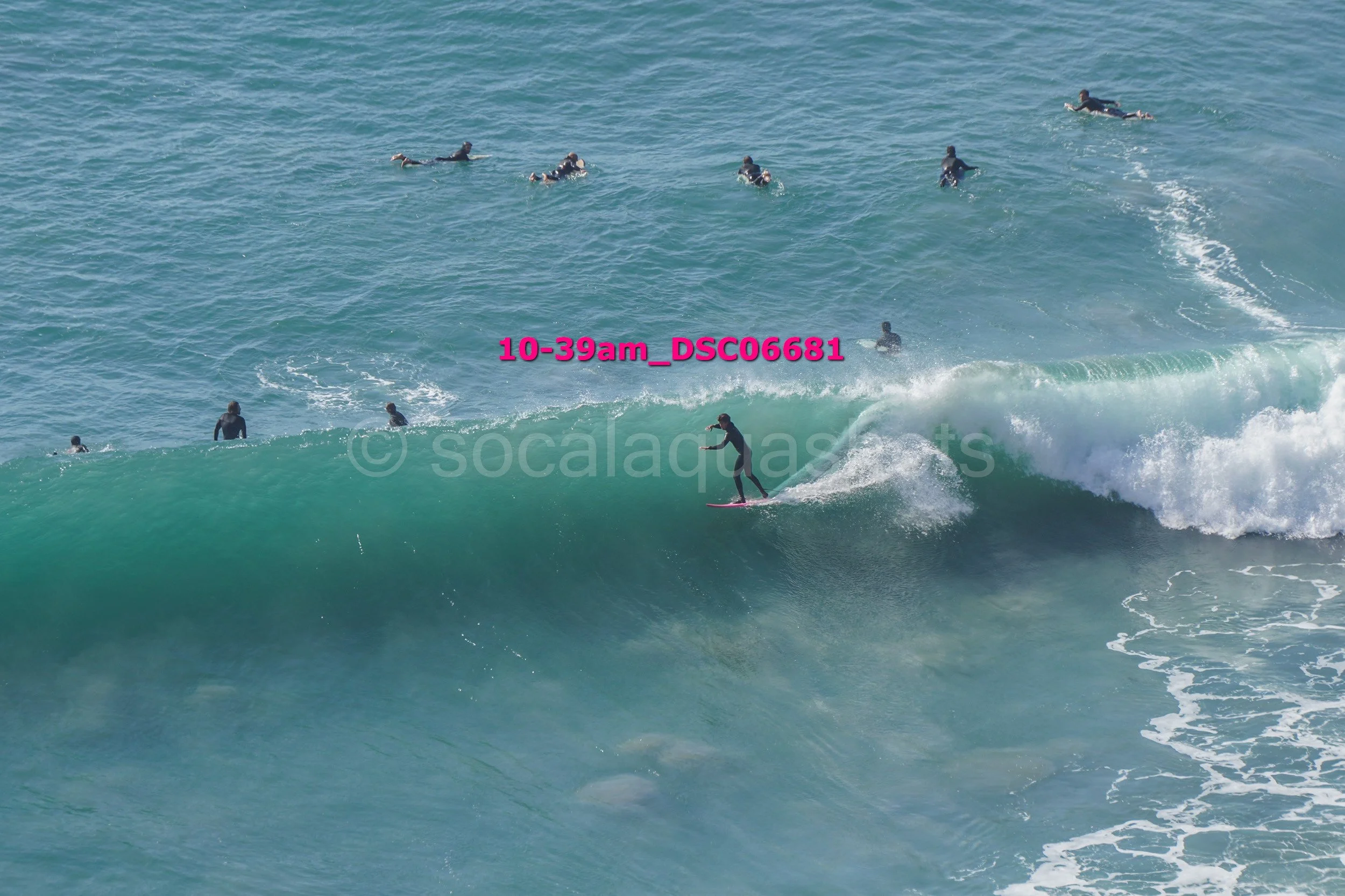 A person surfing a large wave with several other surfers in the water nearby.