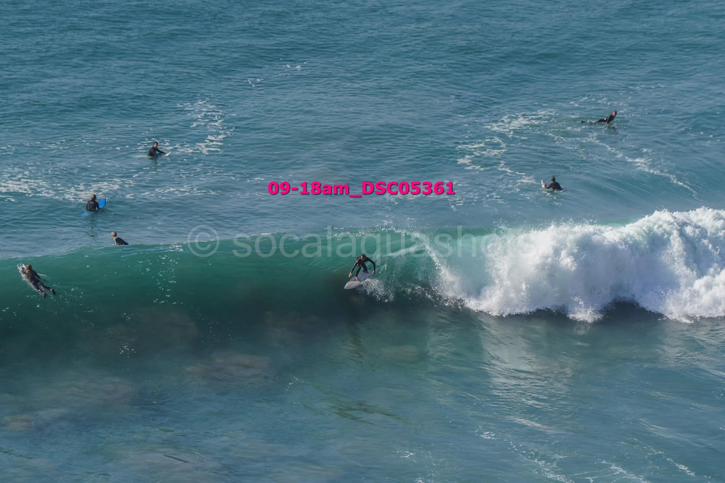 Surfer riding a wave with several surfers waiting in the water nearby.