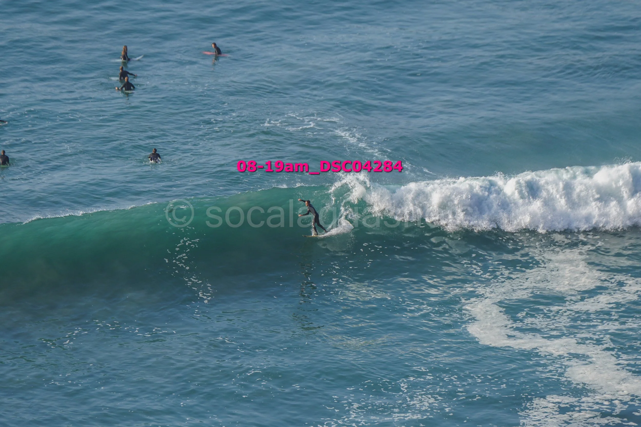 A person surfing on a wave in the ocean with multiple people in the water behind.