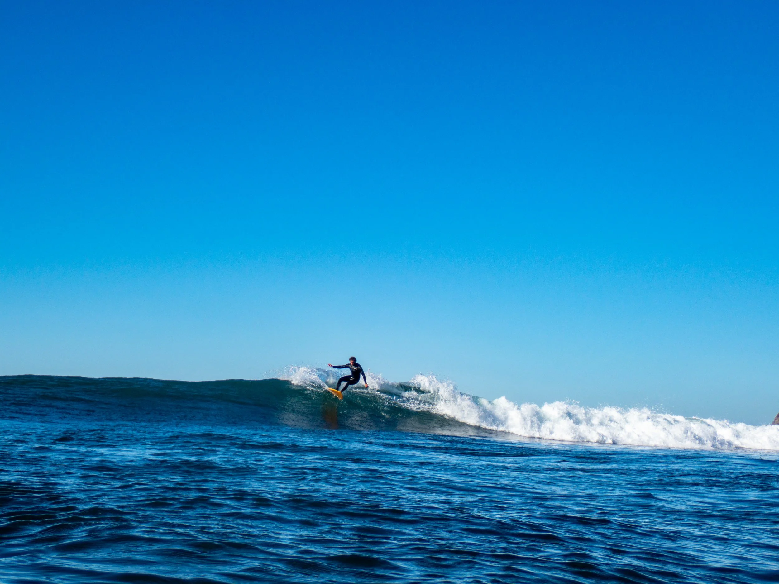 A person surfing on a wave in the ocean with a clear blue sky in the background.