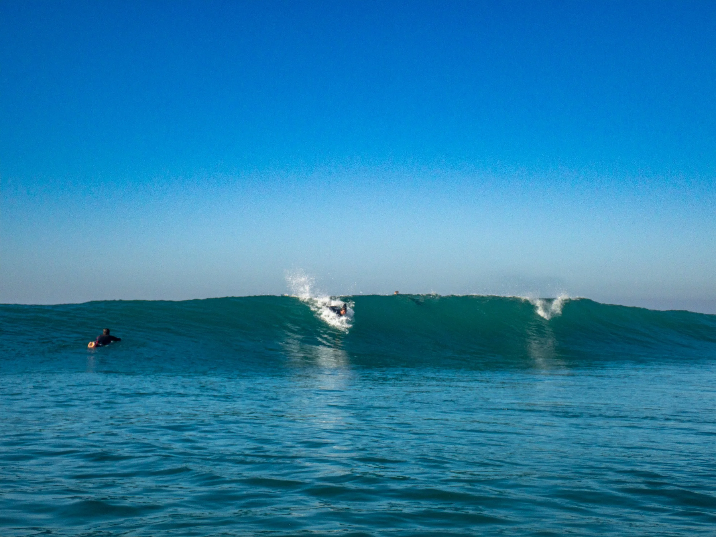A person surfing on a wave in the ocean with another person floating nearby.