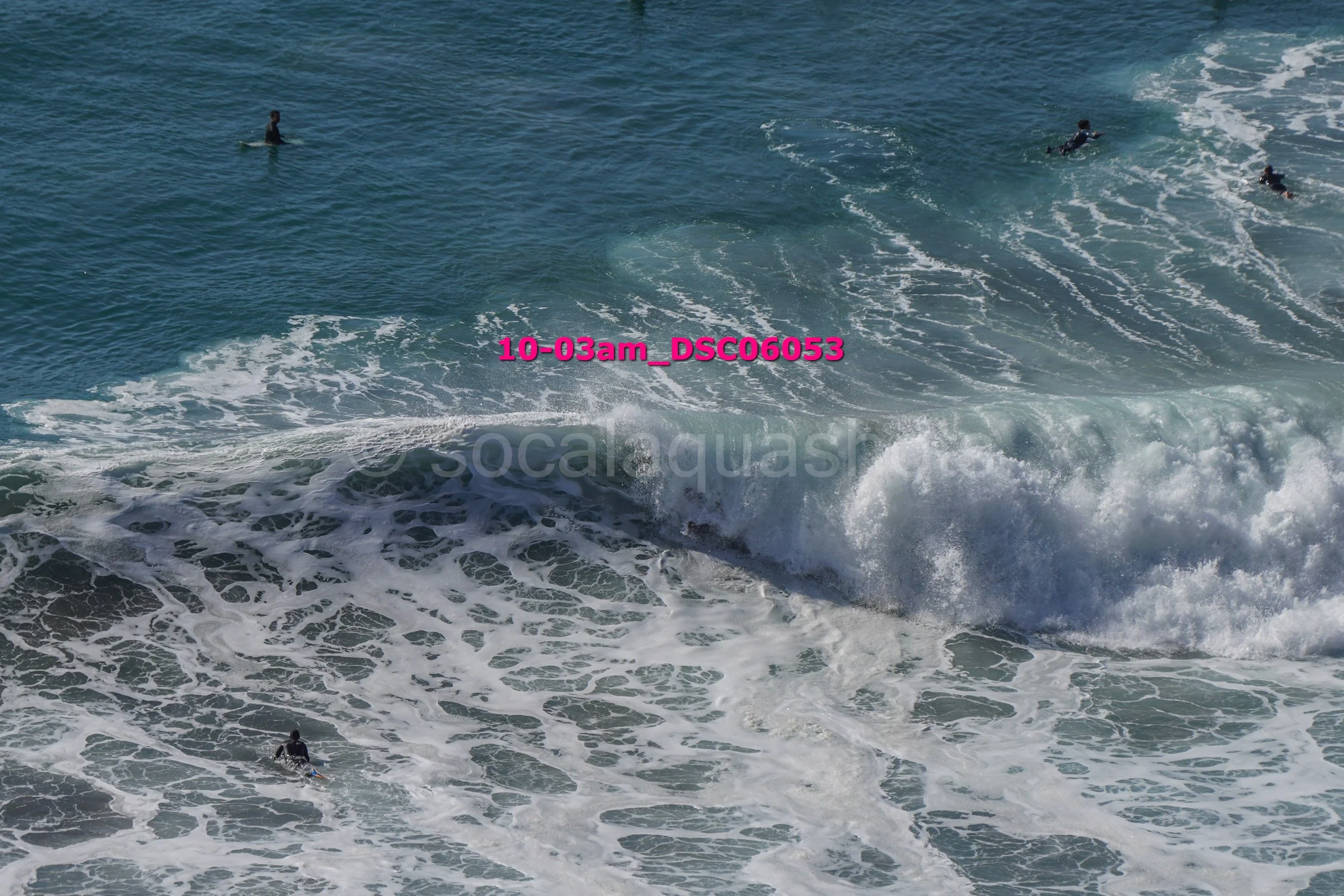 Multiple surfers in the ocean with waves, some waiting and some riding the waves, under clear sky.