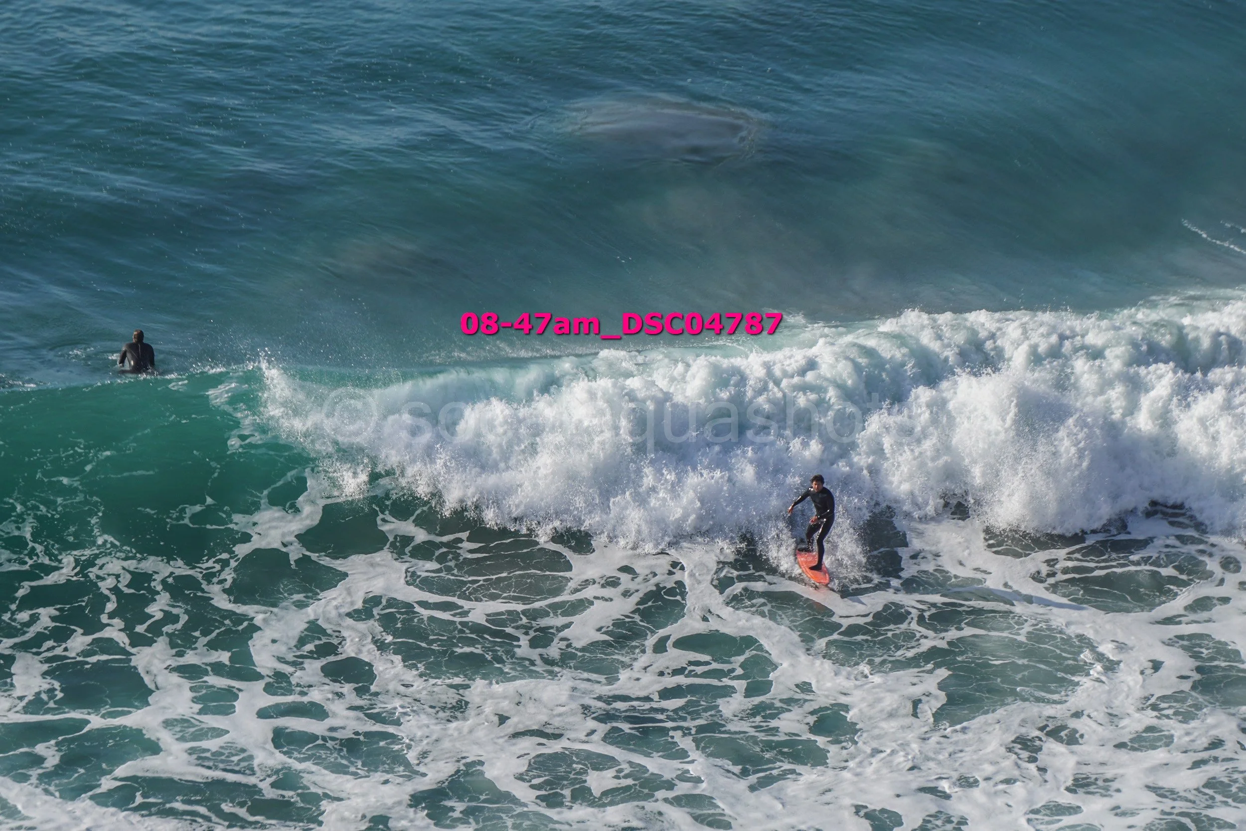 A person surfing on a wave in the ocean with another person swimming nearby.