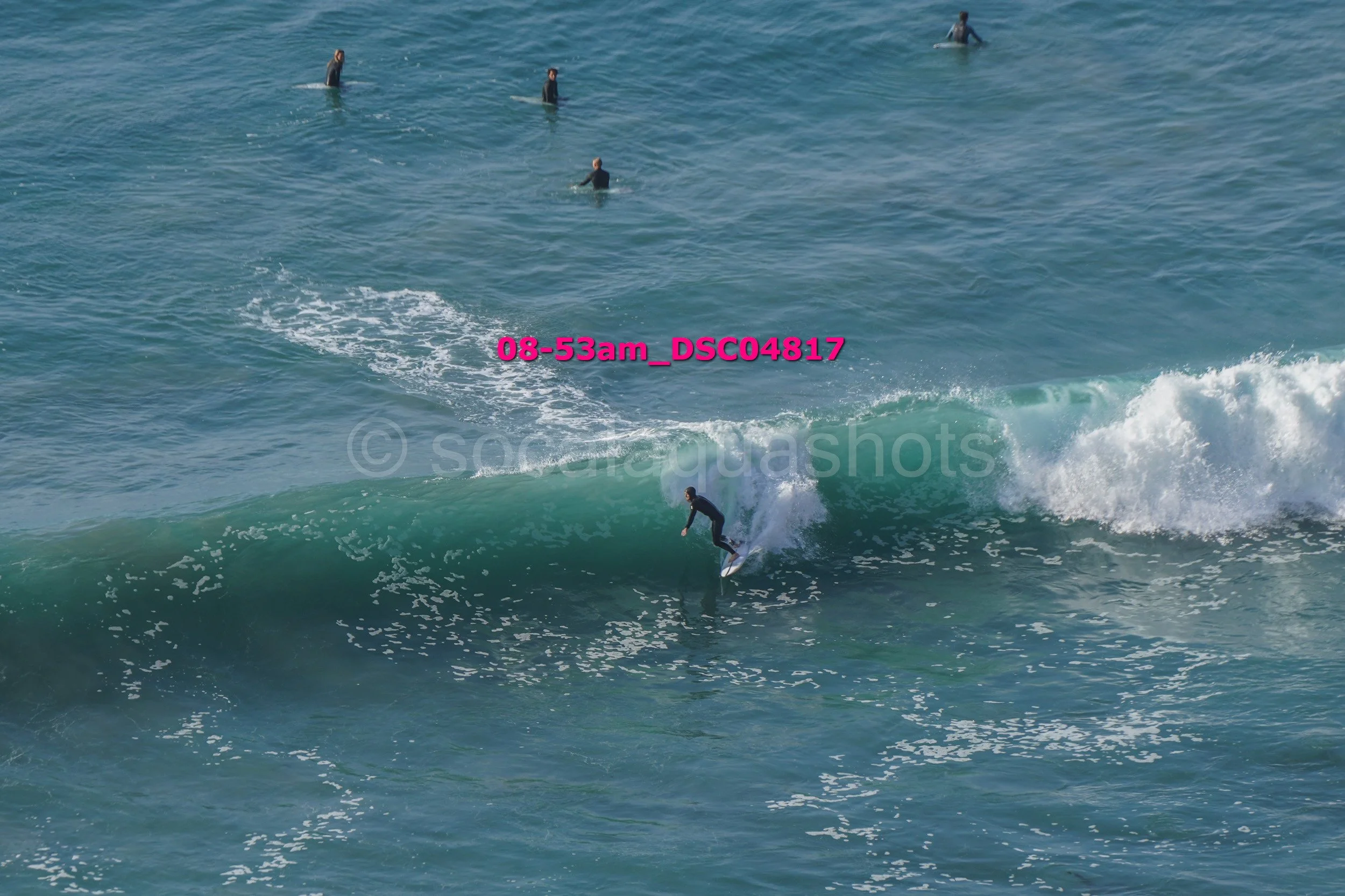 A person surfing on a wave in the ocean with several other individuals in the water in the background.
