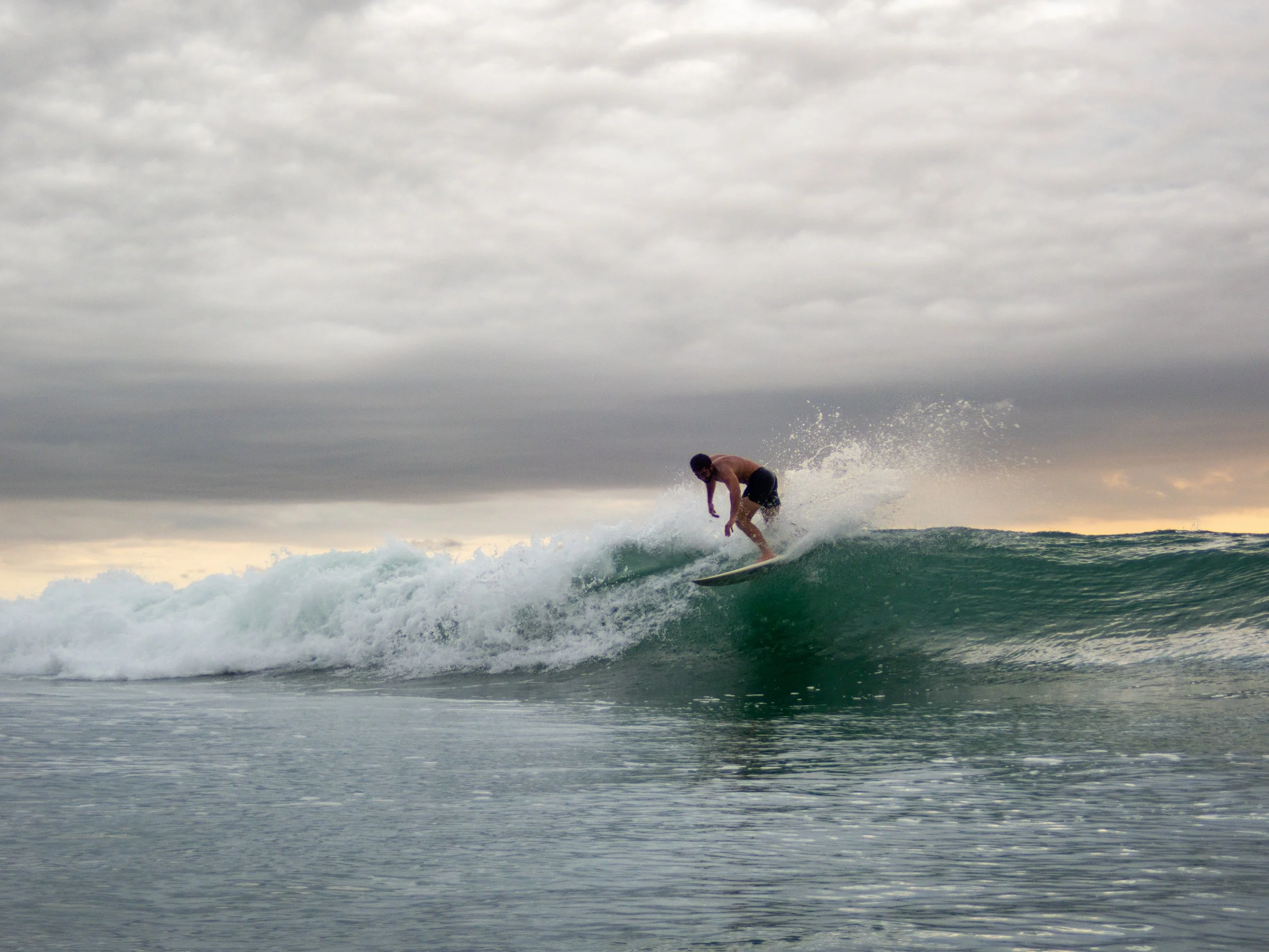 Surfer riding a wave under a cloudy sky