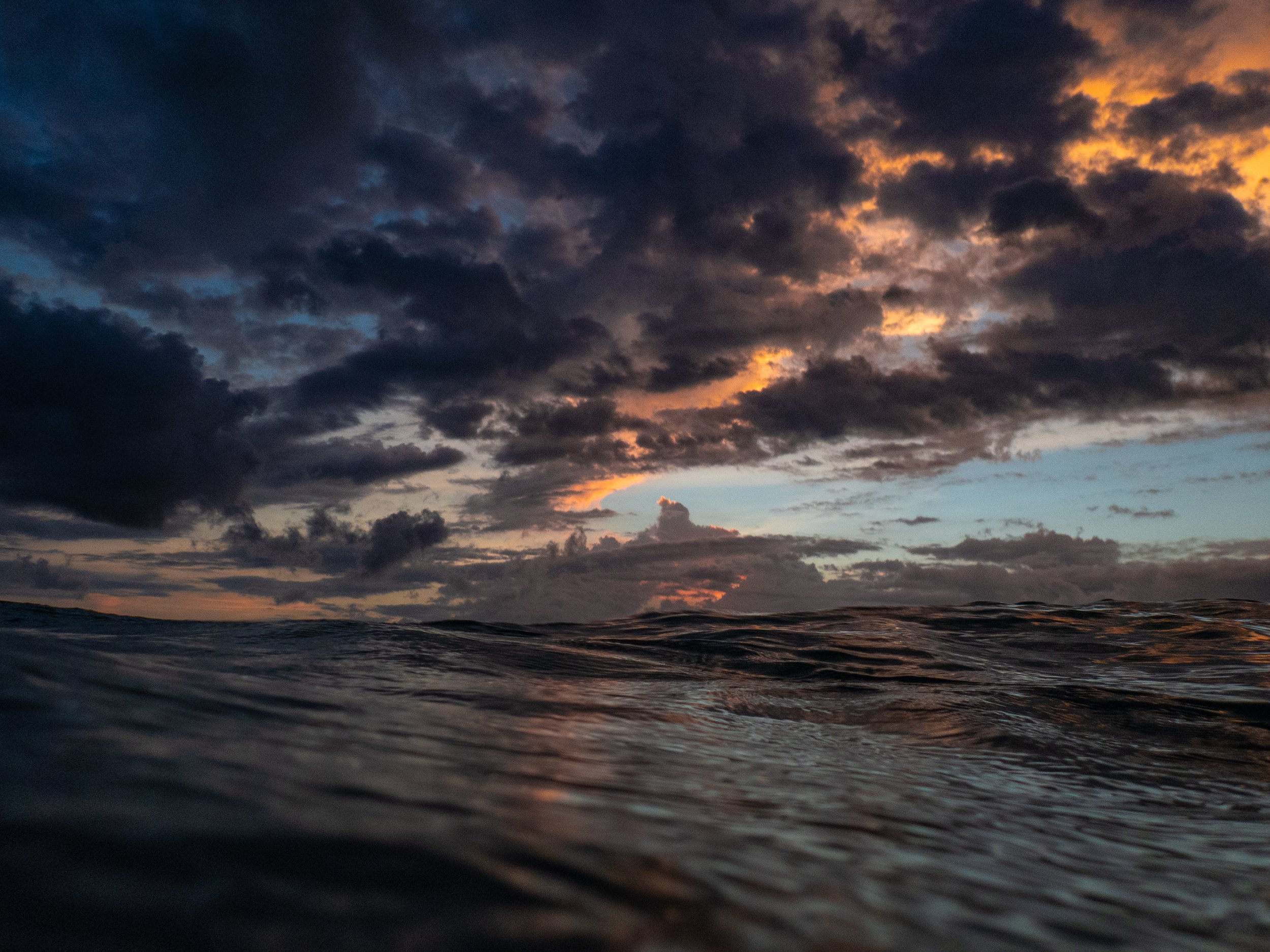 Photo of dark clouds in the sky over the ocean, with a hint of orange and pink glow from the setting sun.