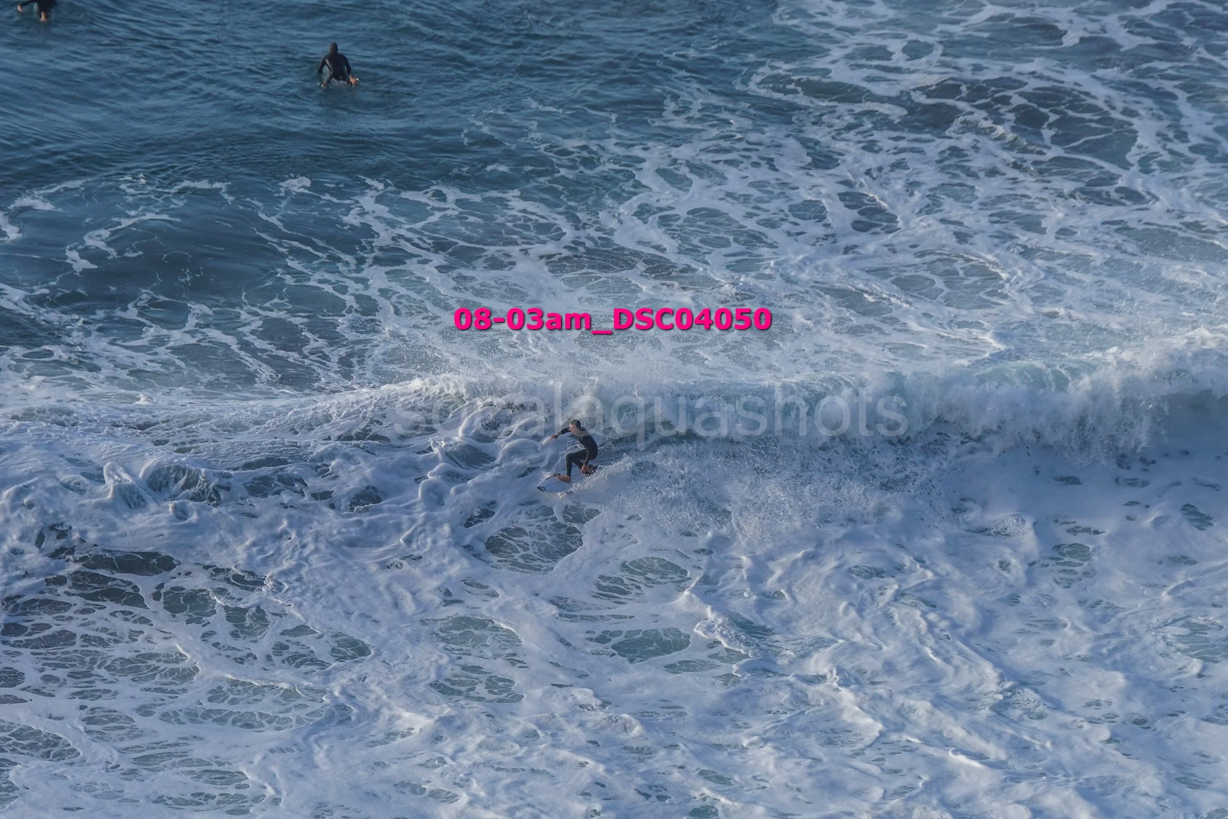 Two surfers riding and paddling in the ocean waves with white foam surface, captured at dawn or early morning.