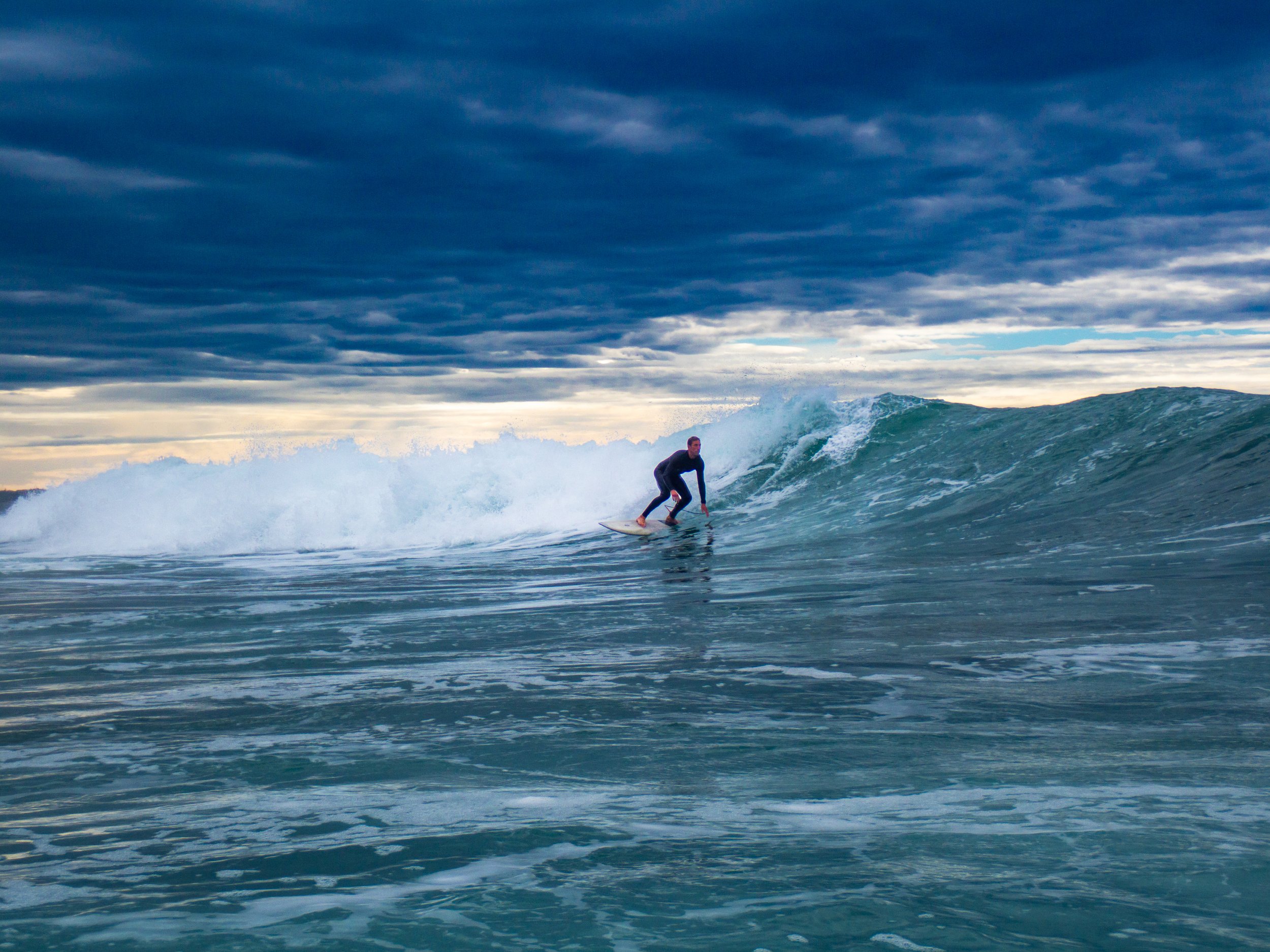 A person surfing on a wave in the ocean under a cloudy sky.