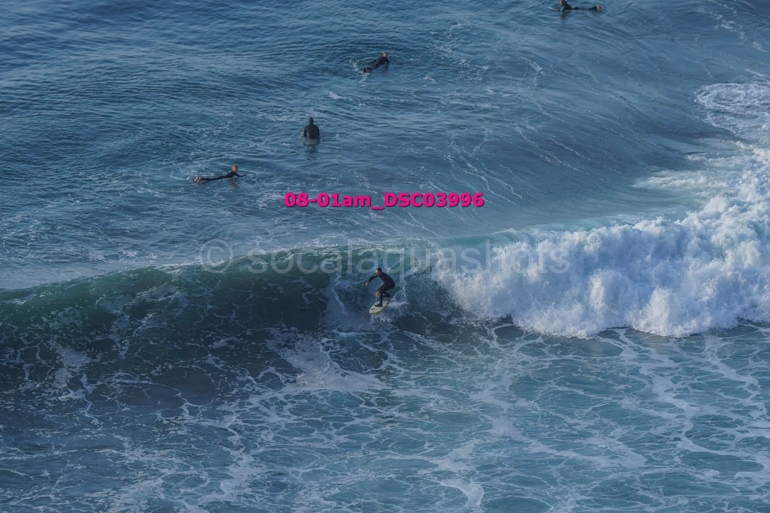 Surfer riding a wave in the ocean with several people swimming behind.